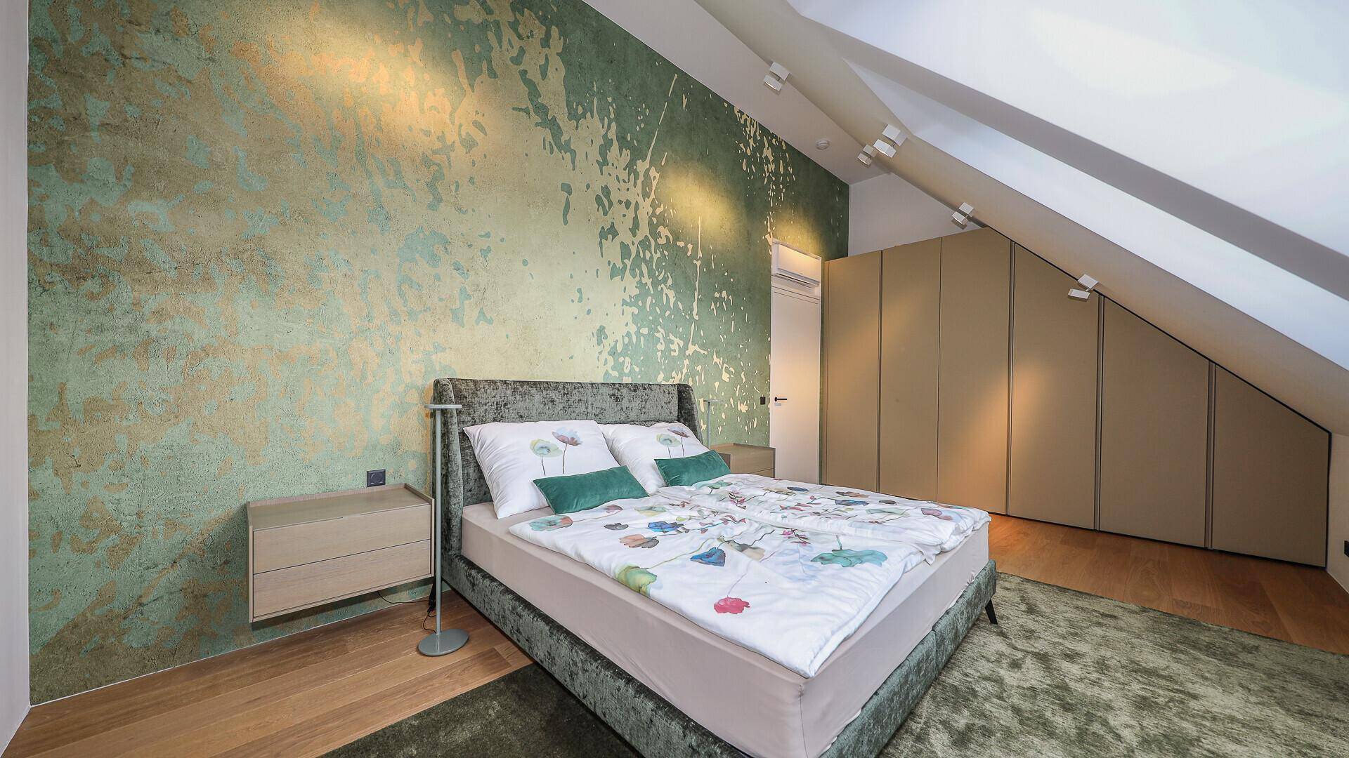 Gemütliches Schlafzimmer im Dachgeschoss mit grüner Akzentwand, Einbauschränken und Holzboden.