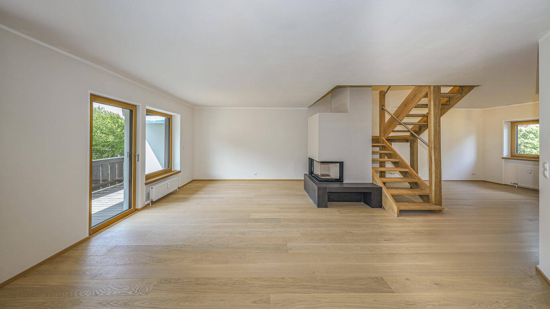 Helles Wohnzimmer mit Zugang zum Balkon, Holzboden, Kamin und offener Holztreppe.