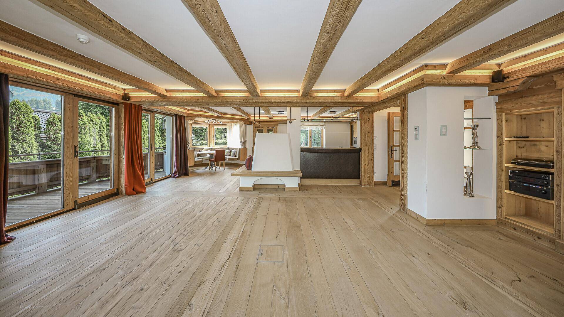 Heller Wohnbereich mit sichtbaren Holzbalken, Kamin und Zugang zu den Terrassen.