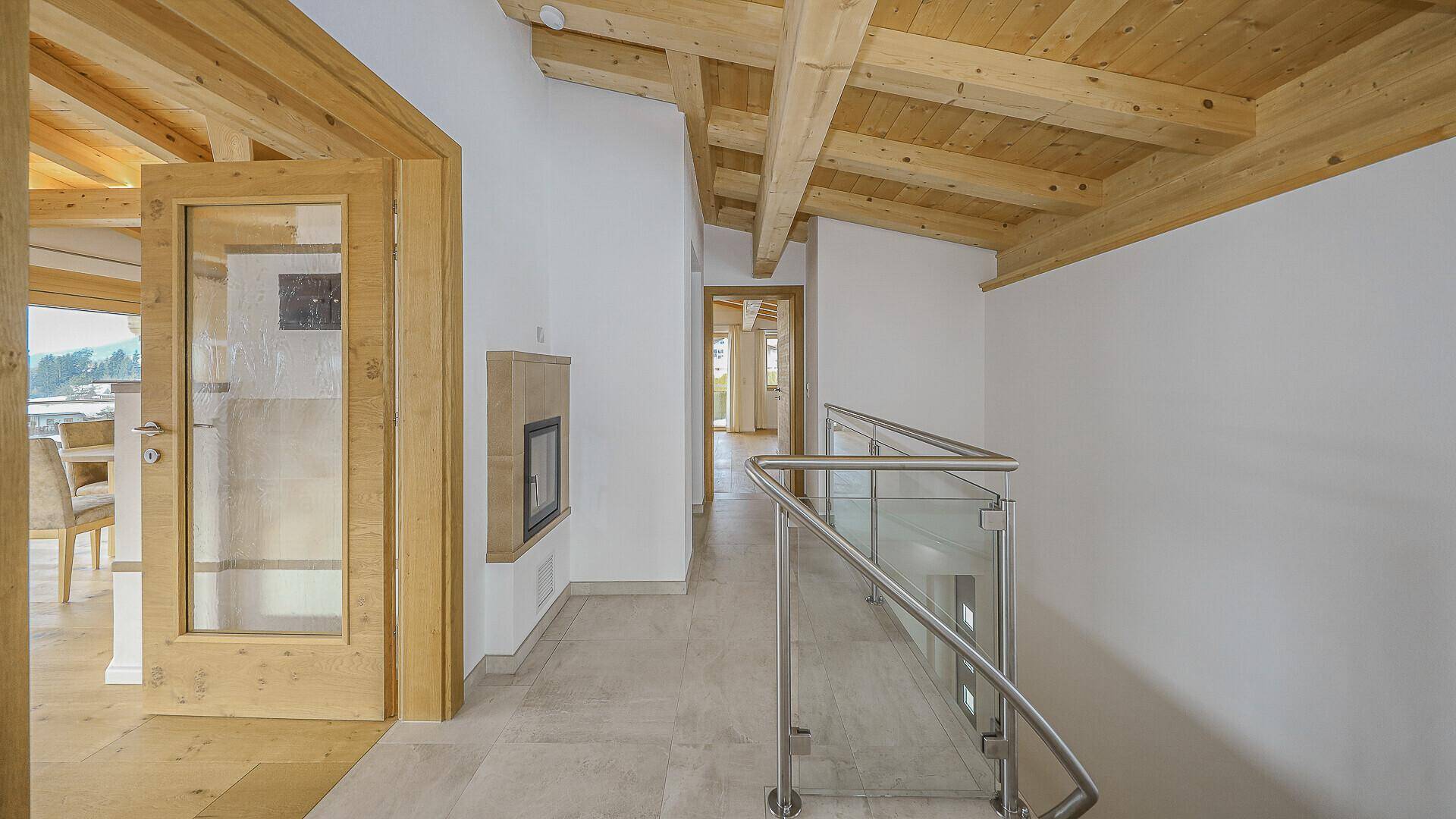 Heller Flur mit modernem Kamin, Steinfliesen und Treppe mit Glasgeländer.