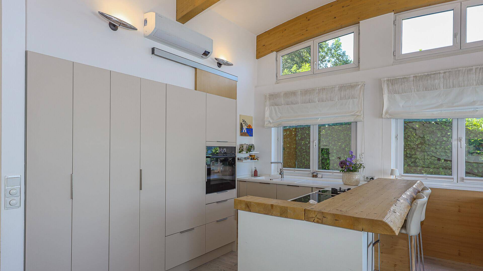 Moderne Einbauküche mit hellen Fronten, Holztheke und großen Fenstern für viel Tageslicht.