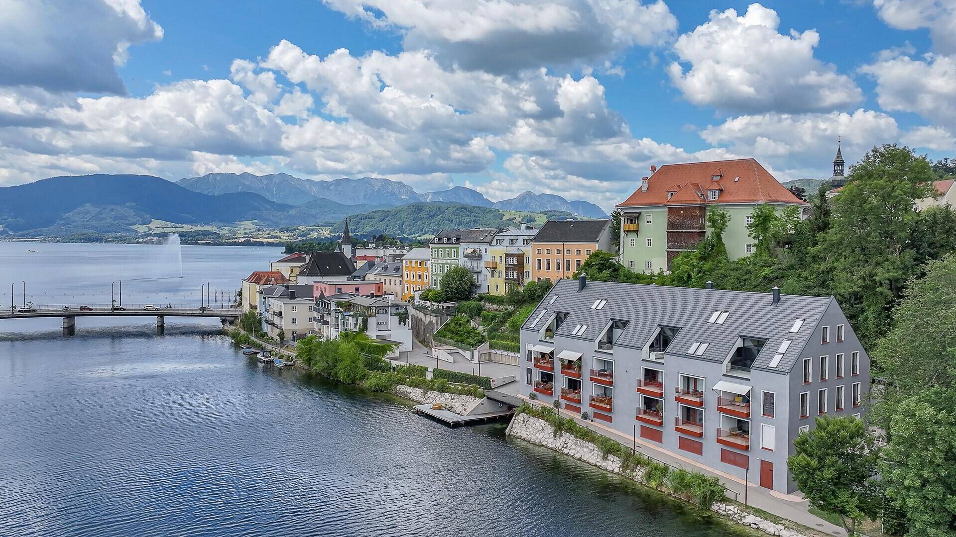 Panoramablick auf die Stadt am See mit Bergen im Hintergrund und dem modernen Gebäude am Ufer.