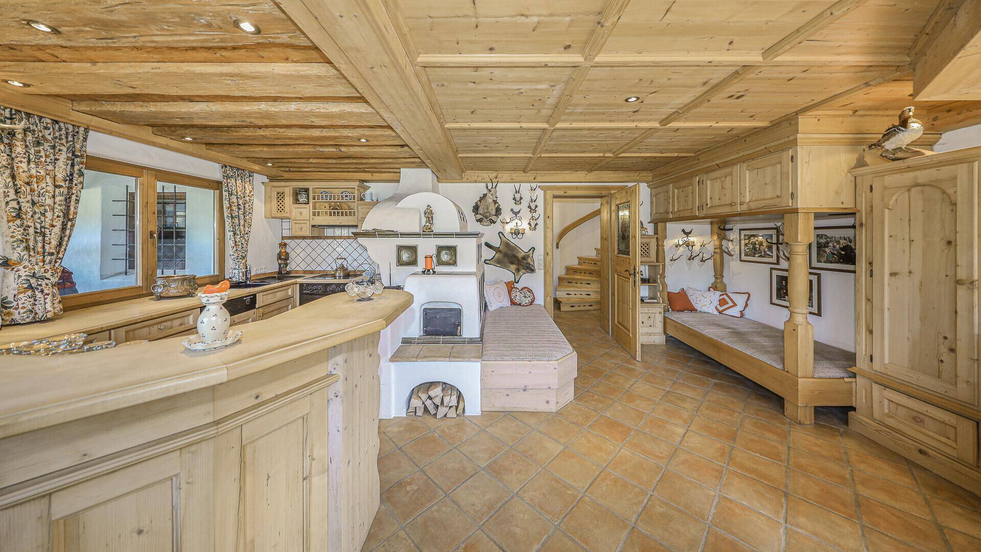 Rustikaler Wohnbereich mit Kachelofen, Bar und integrierter Küche im alpenländischen Stil.