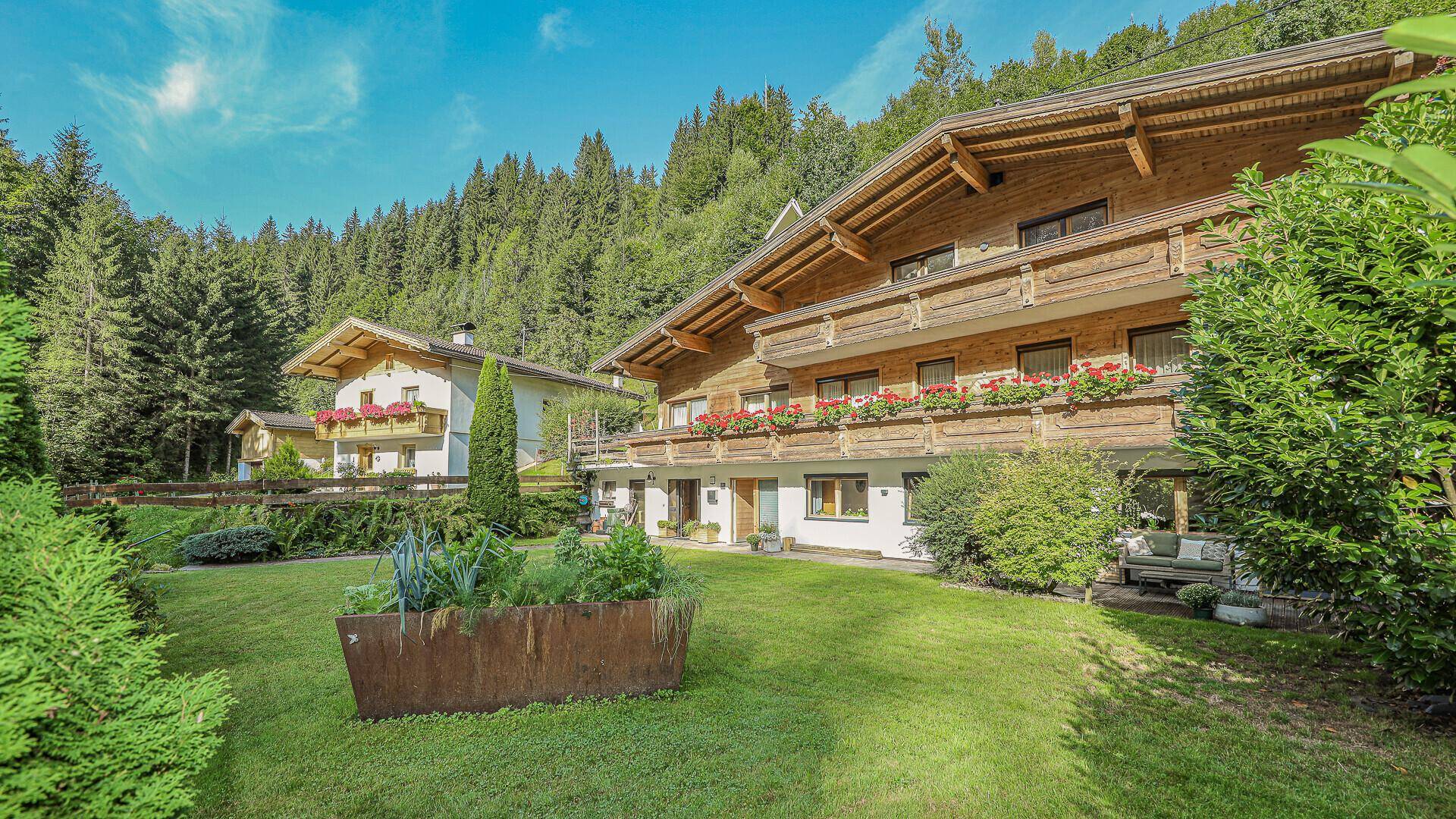 Gepflegter Gartenbereich mit Rasenfläche und Hochbeet vor der traditionellen Holzfassade des Chalets.