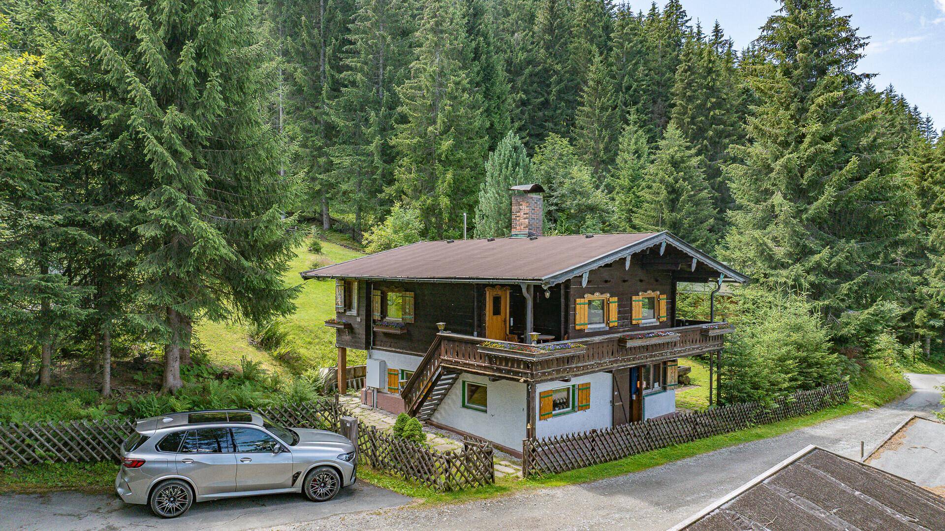 Charmantes Holzhaus mit Balkon und traditionellen Fensterläden, umgeben von üppigem Grün.