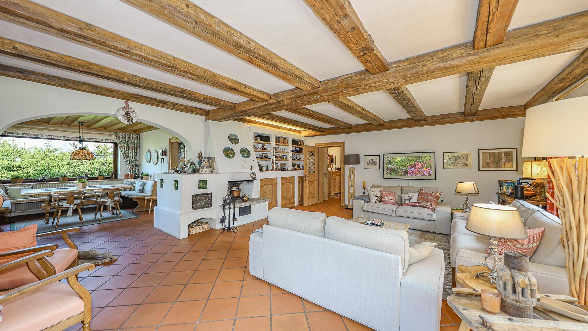 Gemütliches Wohnzimmer im alpinen Stil mit Holzbalkendecke, Kachelofen und Terracotta-Boden.