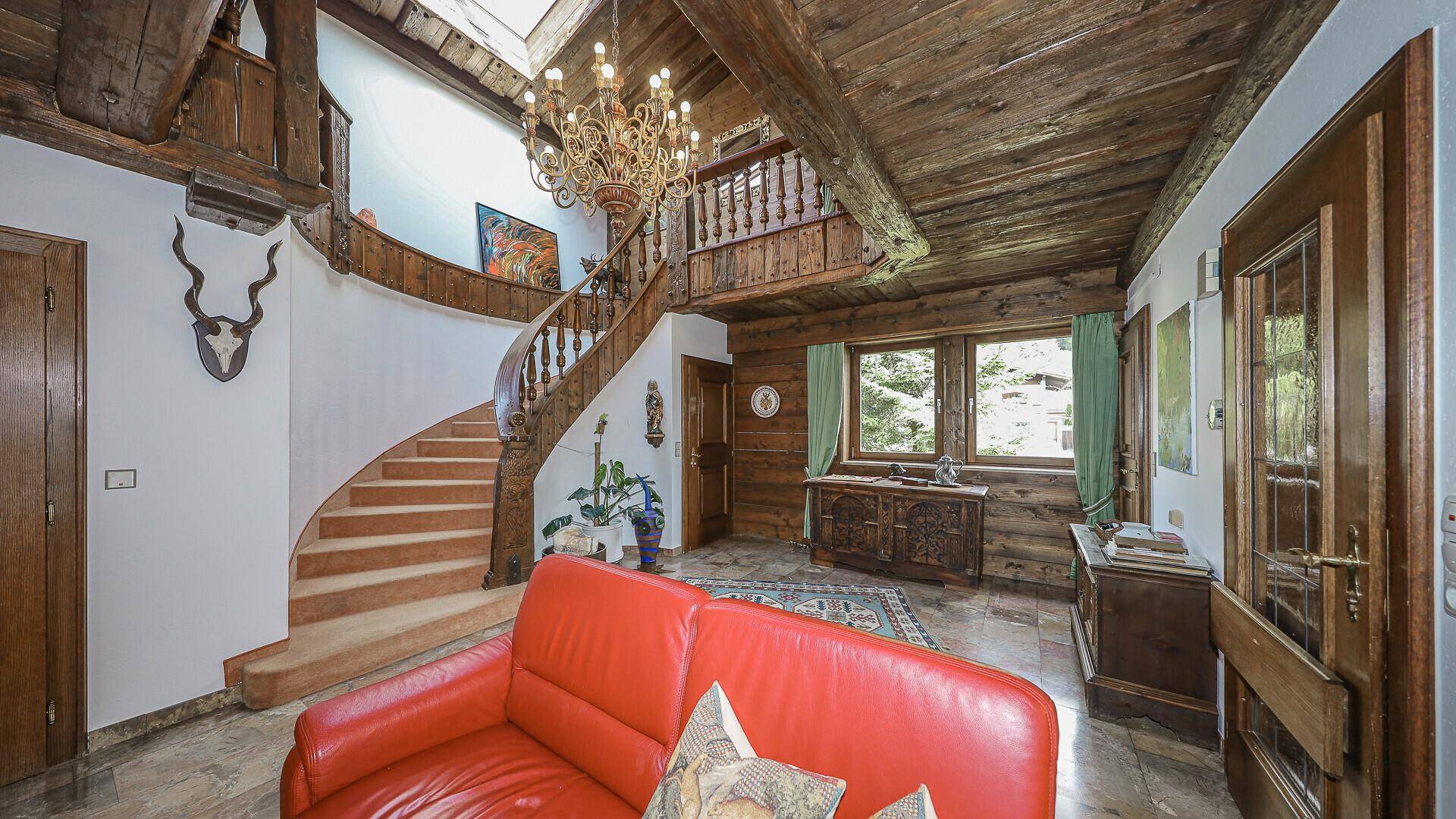 Geräumiger Flur mit geschwungener Holztreppe, Holzbalkendecke und Steinfliesenboden.