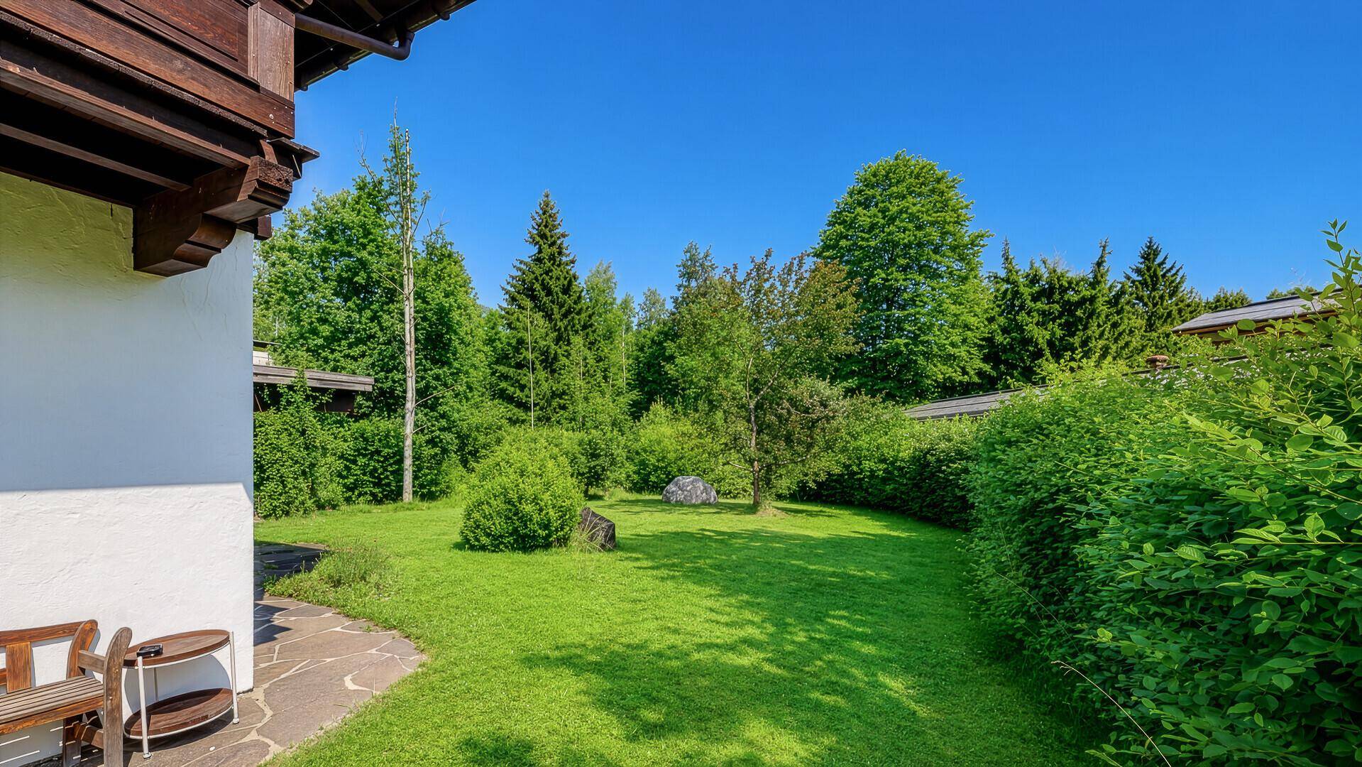 Ruhiger Gartenbereich mit großer Rasenfläche und altem Baumbestand neben dem Haus.