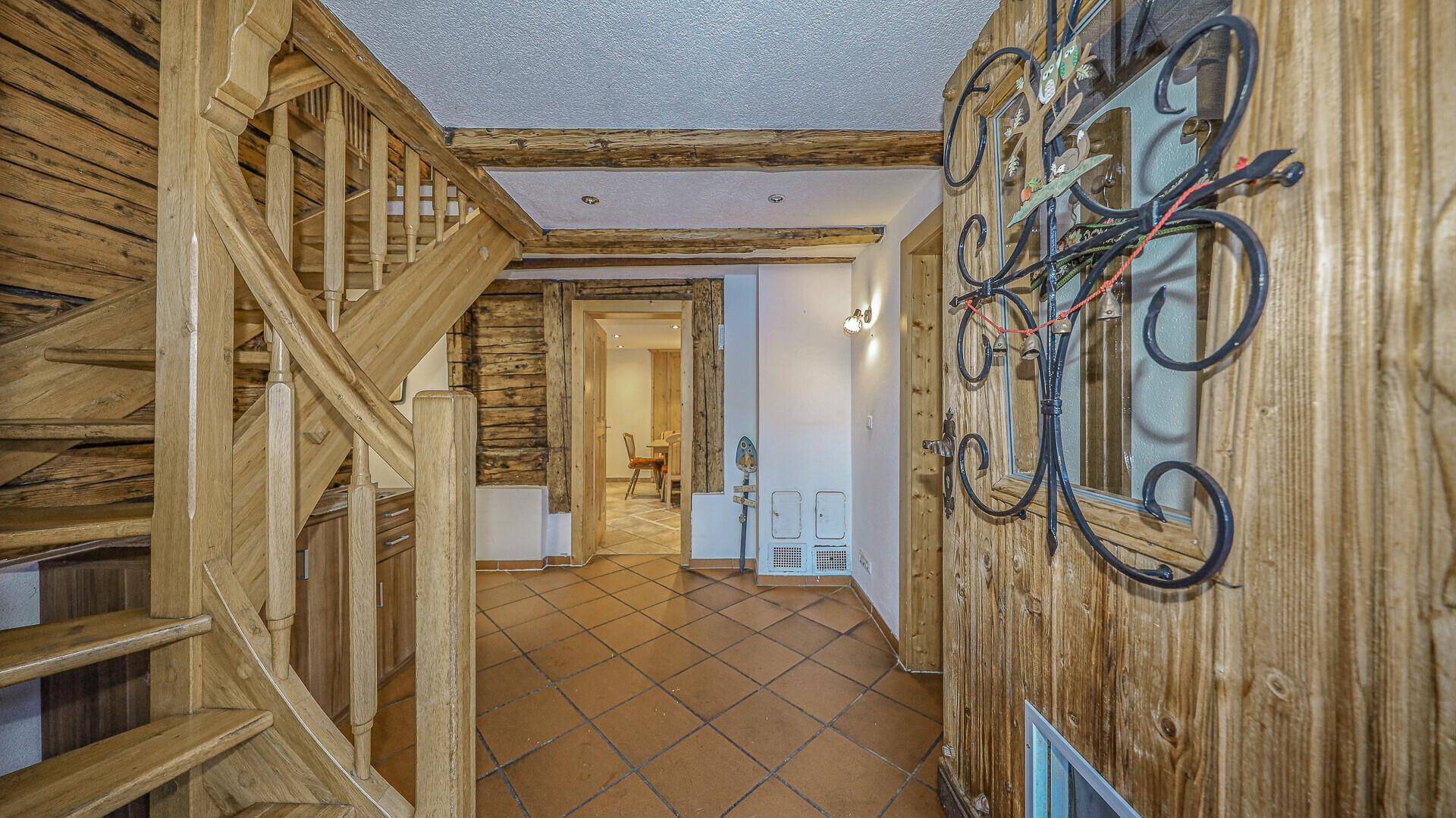 Flur mit Holztreppe, gefliestem Boden und traditioneller Wanddekoration.