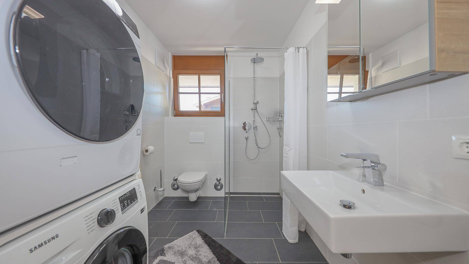 Modernes Badezimmer mit ebenerdiger Dusche, Waschbecken und Waschmaschine.