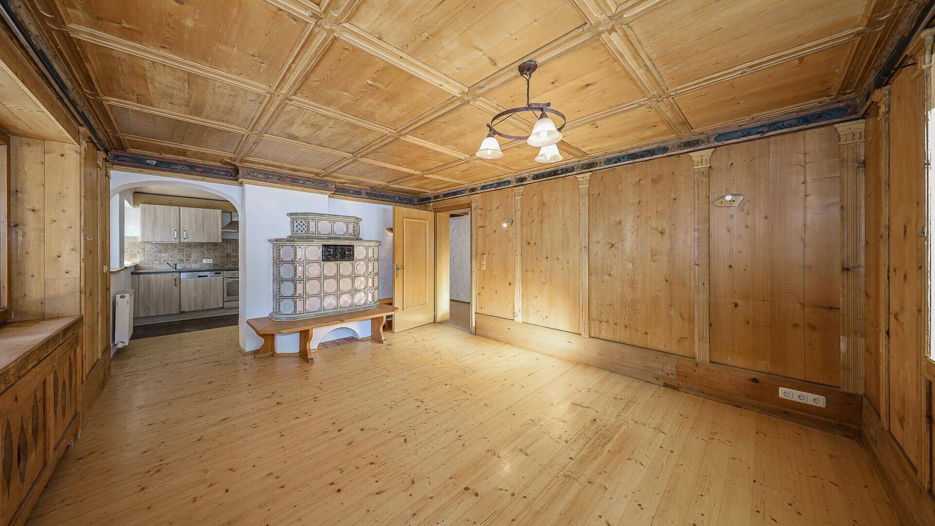 Geräumiger Wohnbereich mit traditioneller Holzvertäfelung, Holzboden und Kachelofen.