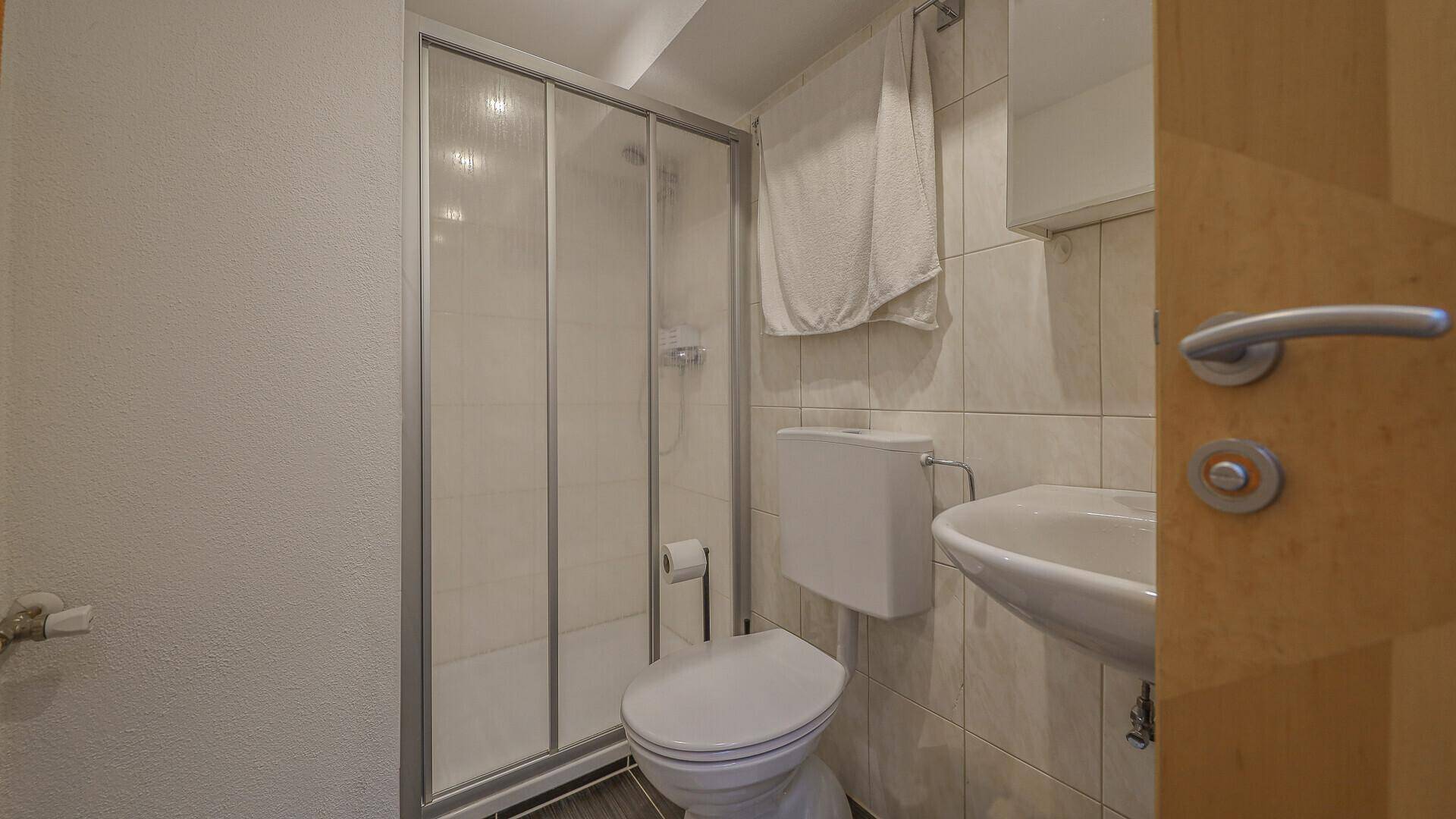 Helles Badezimmer mit Dusche, WC und Waschbecken, ausgestattet mit weißen Fliesen.