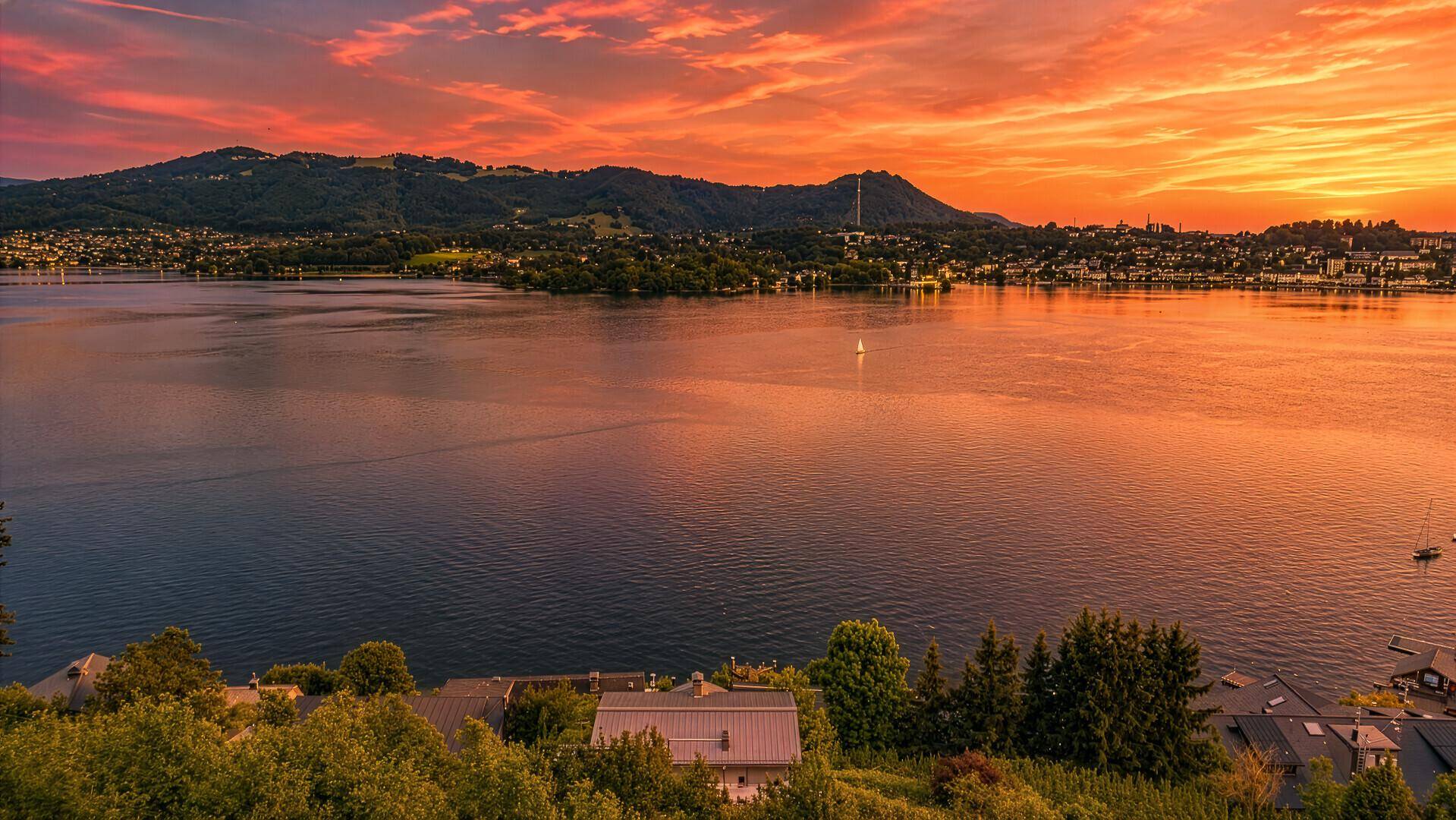 Panoramablick auf einen See bei Sonnenuntergang, umgeben von Bergen und einer malerischen Landschaft.