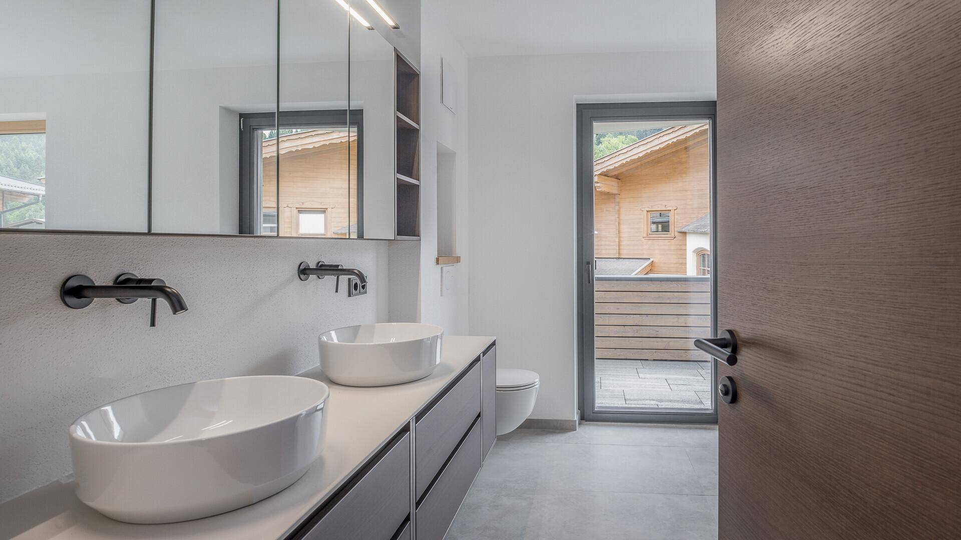 Modernes Badezimmer mit Doppelwaschbecken, Spiegelschrank und Zugang zu einem Außenbereich.