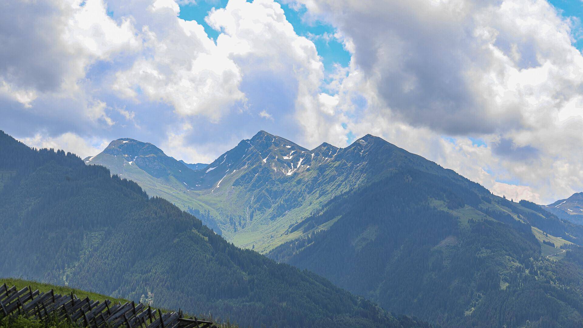 Majestätische Berggipfel mit schneebedeckten Flanken unter einem bewölkten Himmel.