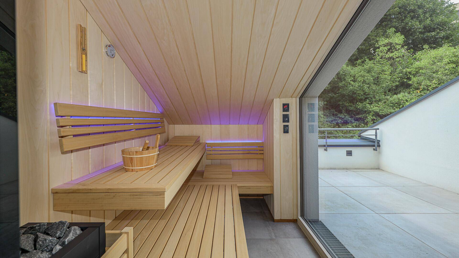 Moderne Sauna mit Holzverkleidung, indirekter Beleuchtung und Zugang zur Außenterrasse.