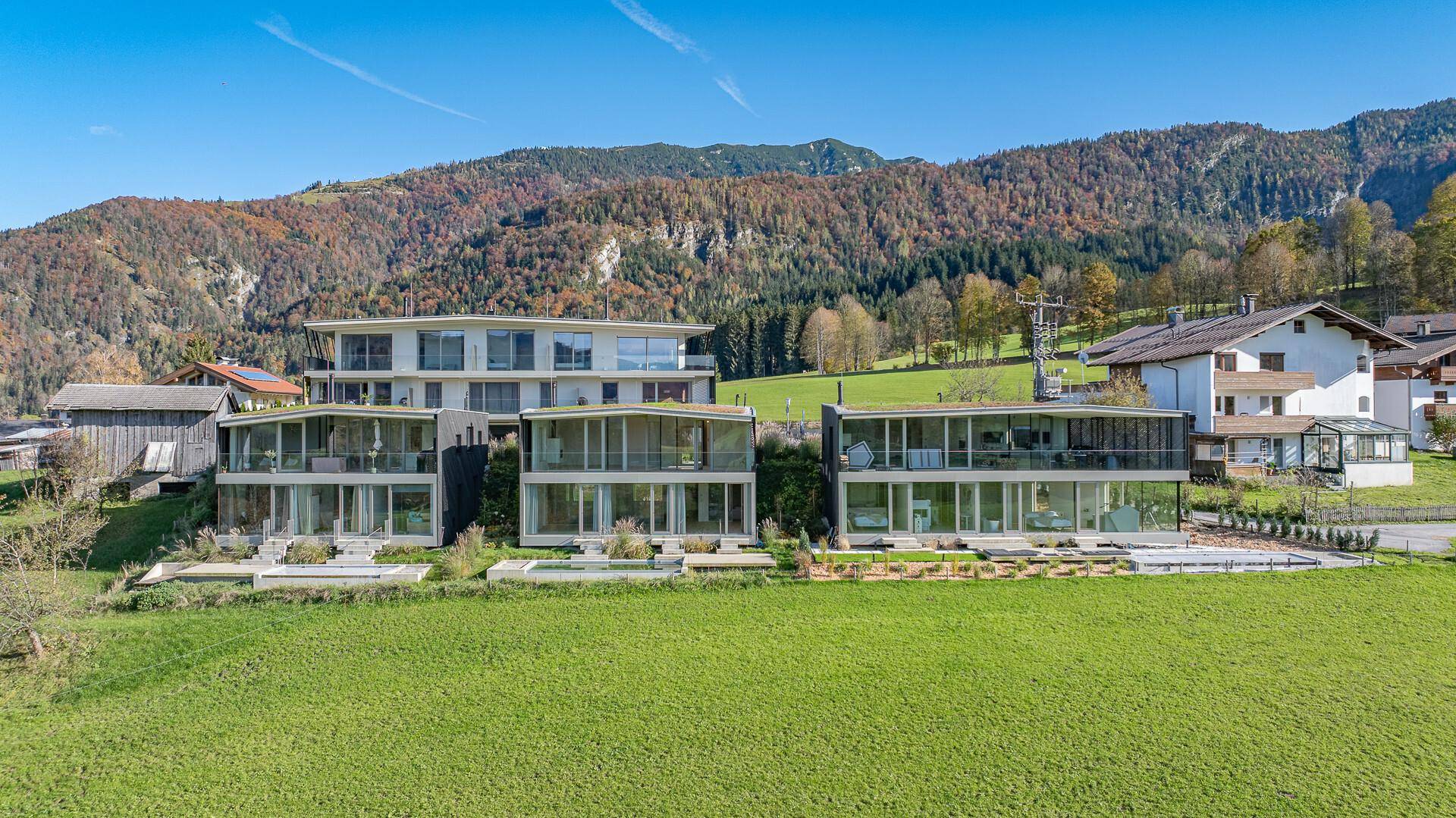 Weitläufige Ansicht des modernen Gebäudekomplexes mit Glasfassaden, eingebettet in eine grüne Berglandschaft.