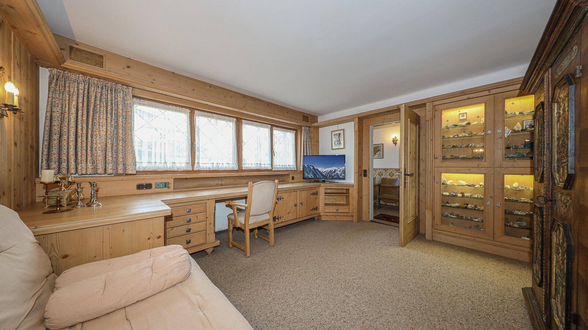 Gemütliches Arbeitszimmer mit Holzvertäfelung, Schreibtisch und Vitrinenschrank im traditionellen Stil.