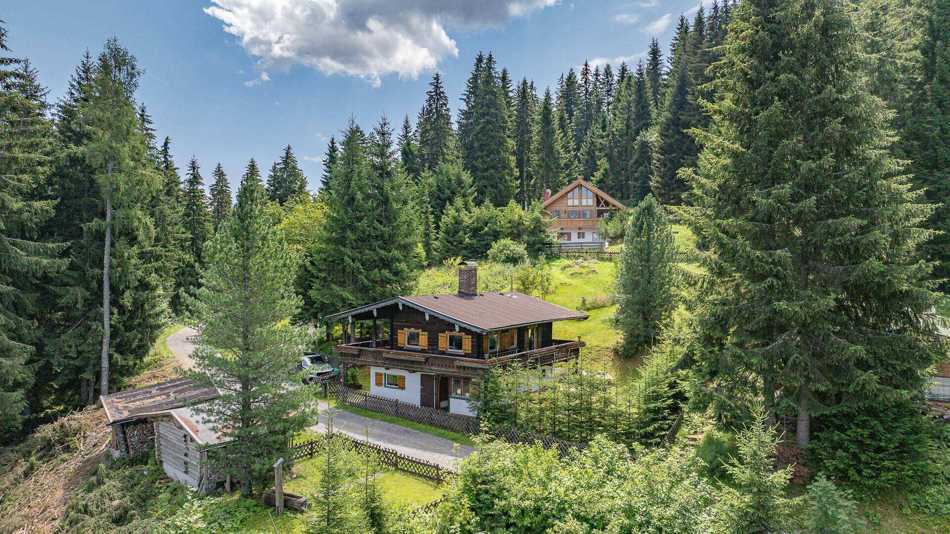 Traditionelles Holzchalet umgeben von dichten Nadelwäldern, mit einem weiteren Gebäude im Hintergrund.