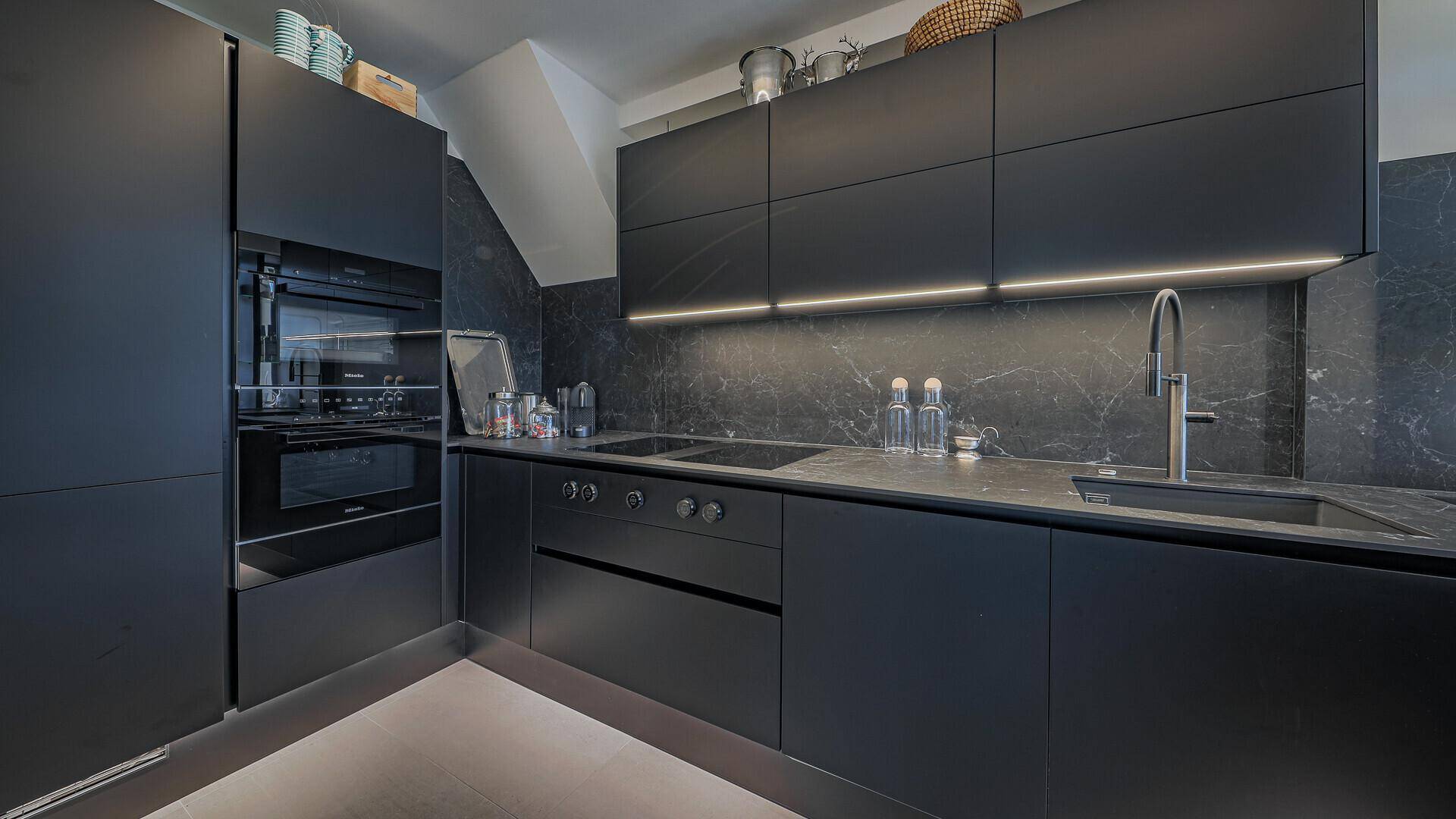 Moderne schwarze Küche mit integrierten Geräten, dunklen Arbeitsplatten und indirekter Beleuchtung.