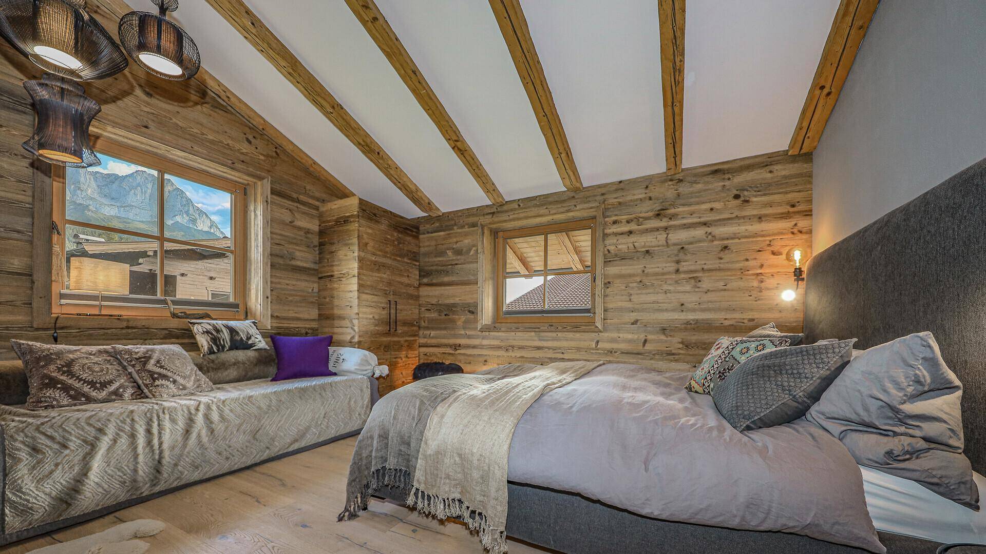 Schlafzimmer mit Holzwänden, Dachschrägen und Blick auf die Berge durch das Fenster.