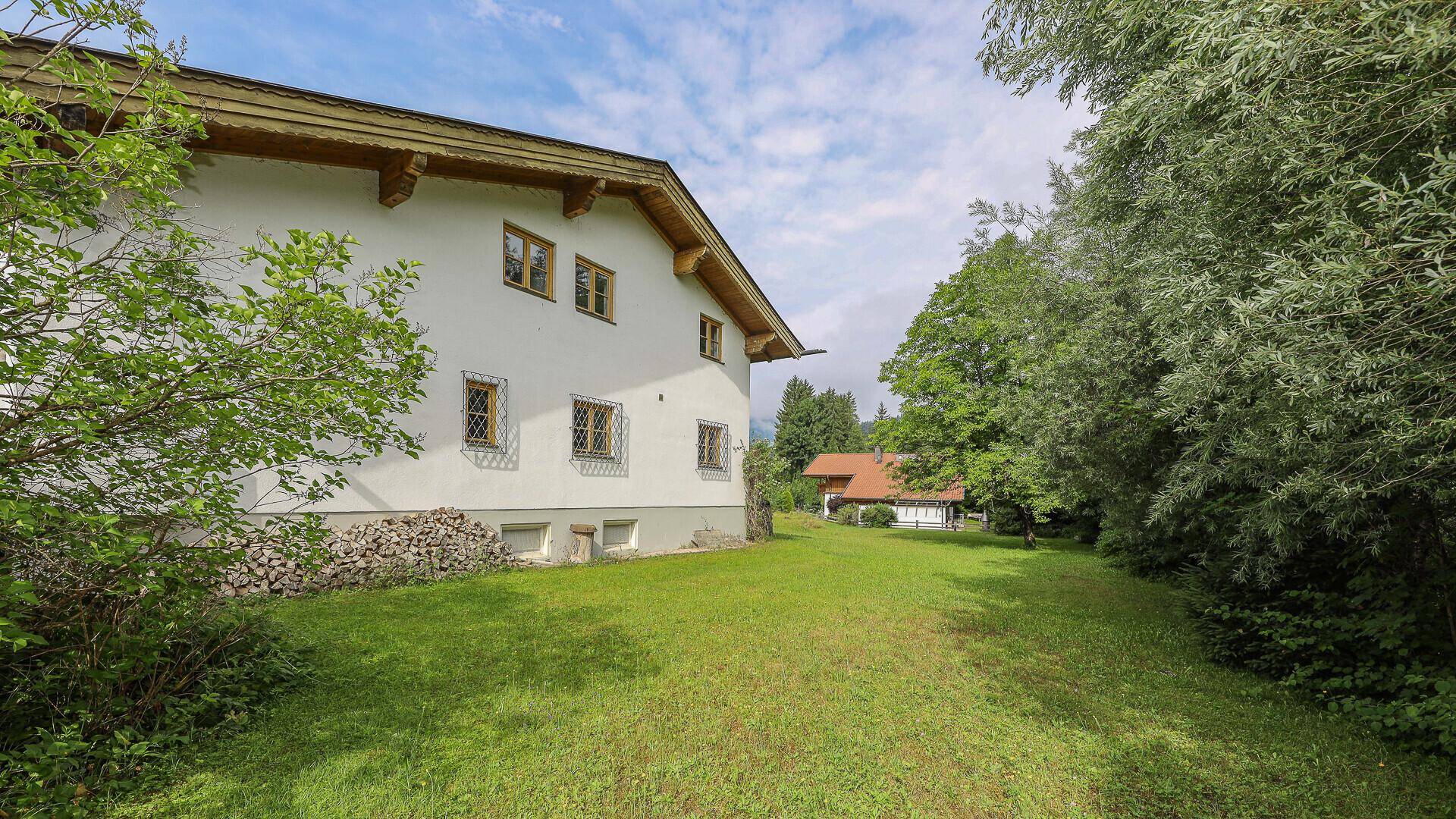 Großer, gepflegter Gartenbereich neben dem Haus mit viel Grün und Holzstapeln.