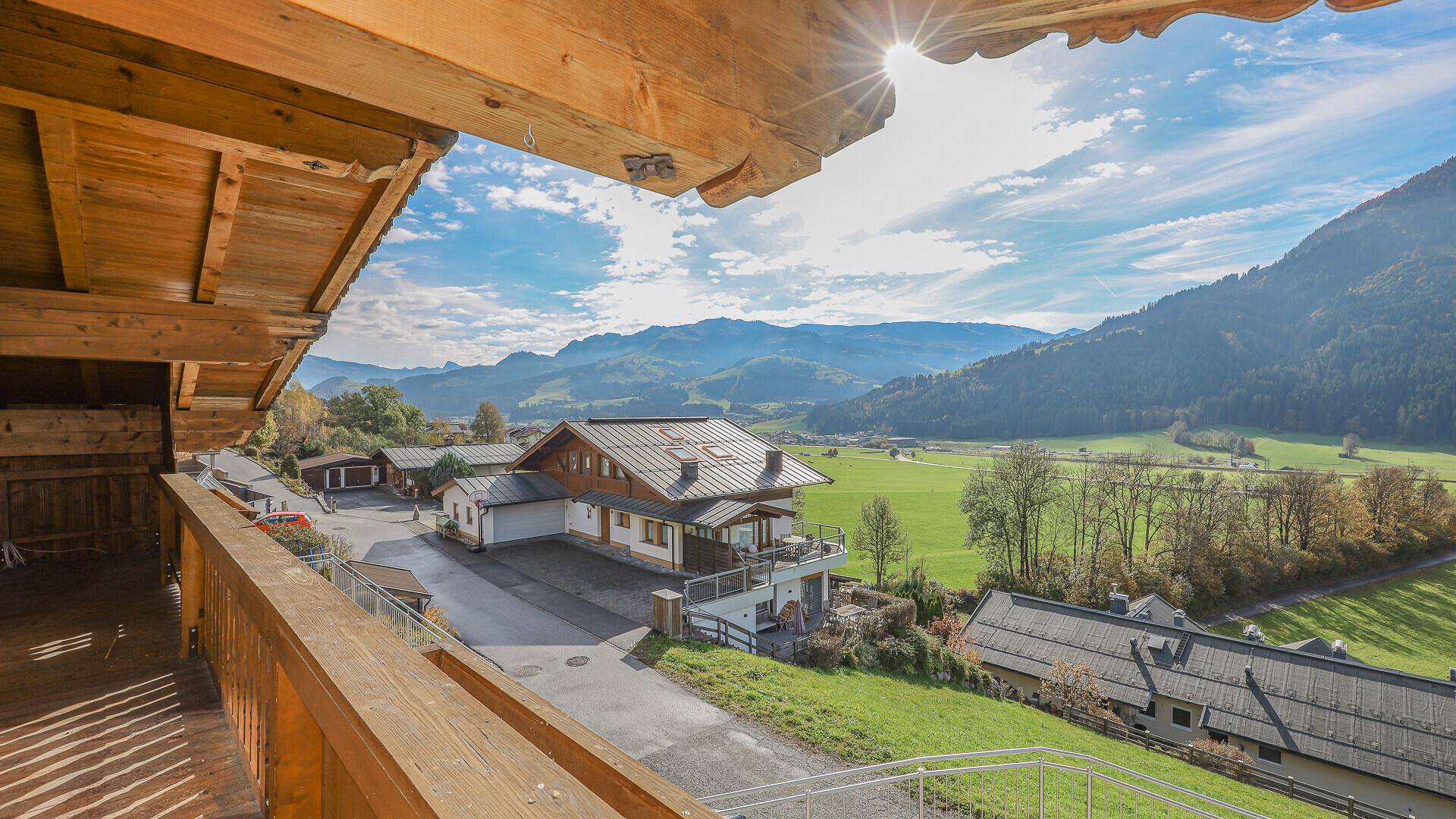 Blick vom Holzbalkon über das Tal mit weiteren Häusern und der beeindruckenden Bergkulisse.