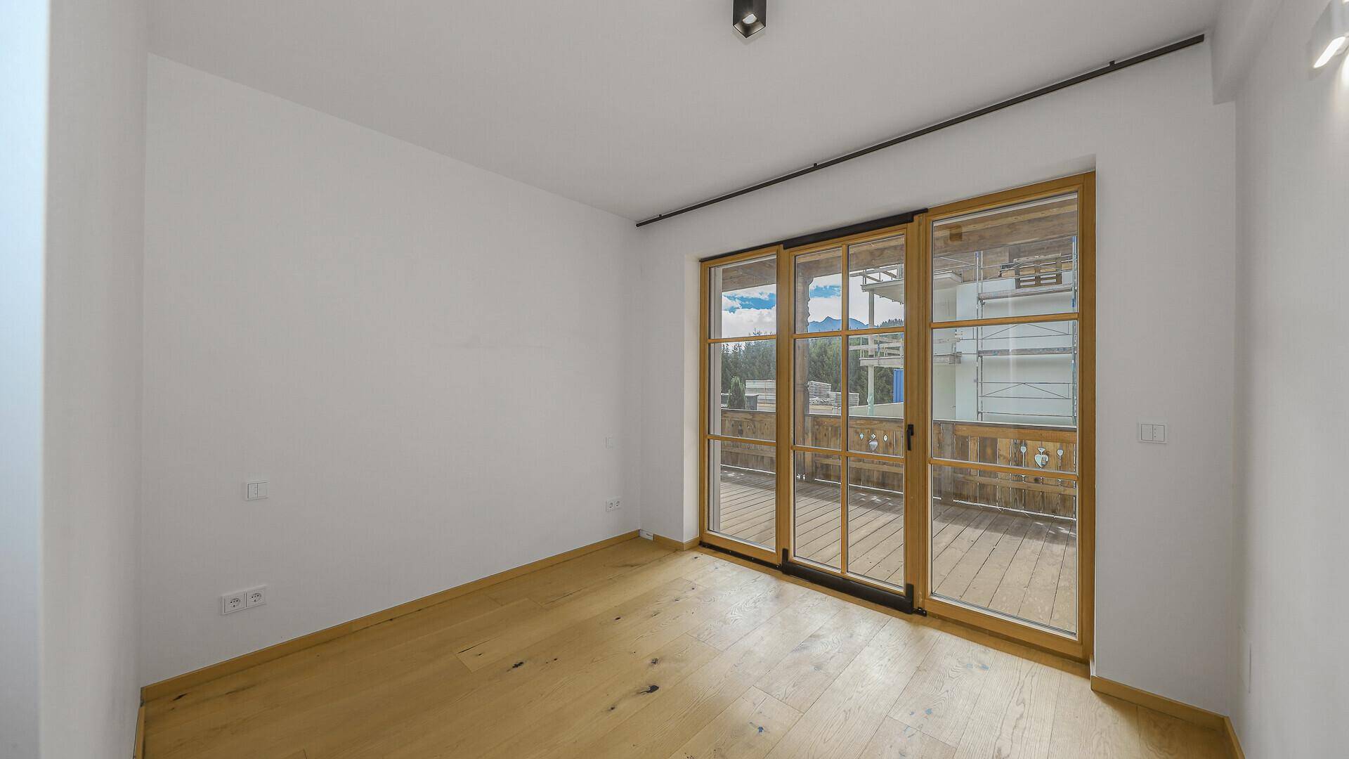 Leeres Schlafzimmer mit Holzboden und Zugang zu einem Balkon.