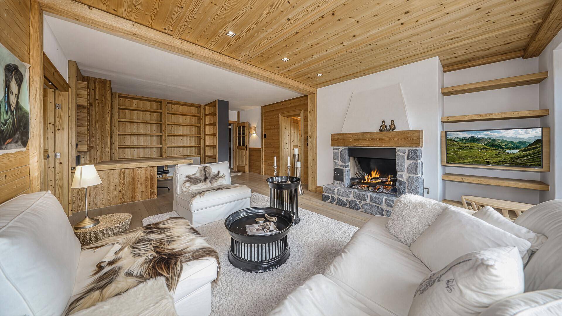 Wohnzimmer mit Kamin, Bücherregalen und bequemen Sofas, alles im warmen Holzdesign.