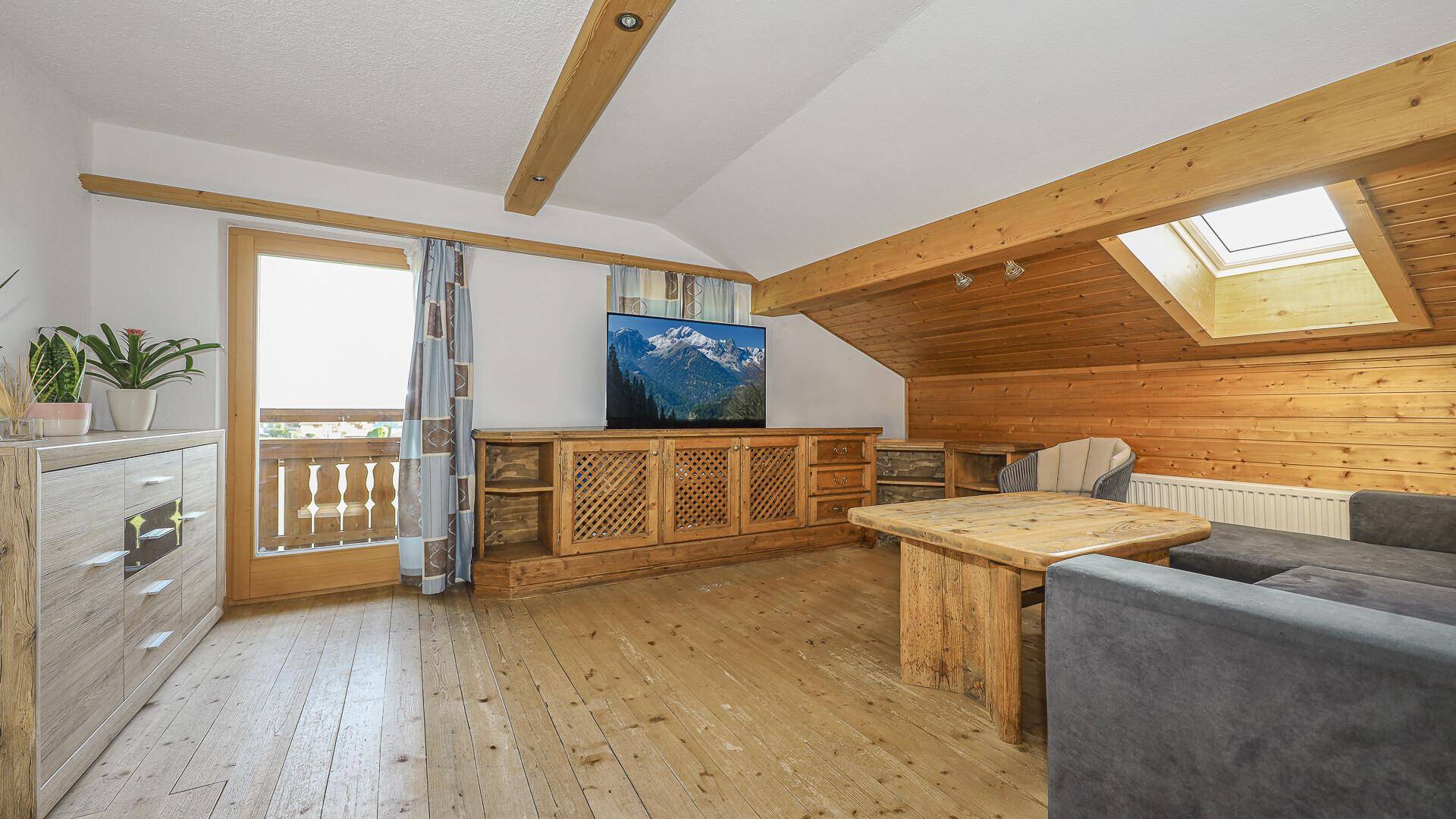 Gemütliches Wohnzimmer im Dachgeschoss mit Holzbalken, Dachfenster und Balkonzugang.