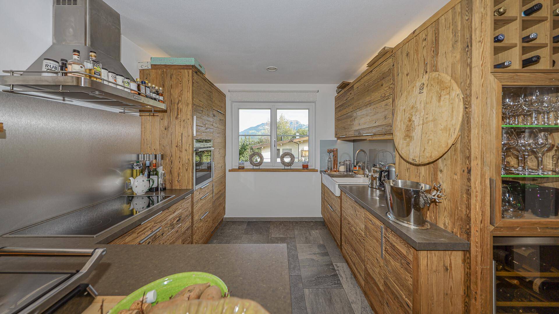 Geräumige Holzküche im Landhausstil mit Spülbecken, Weinkühler und Blick auf die Berge.