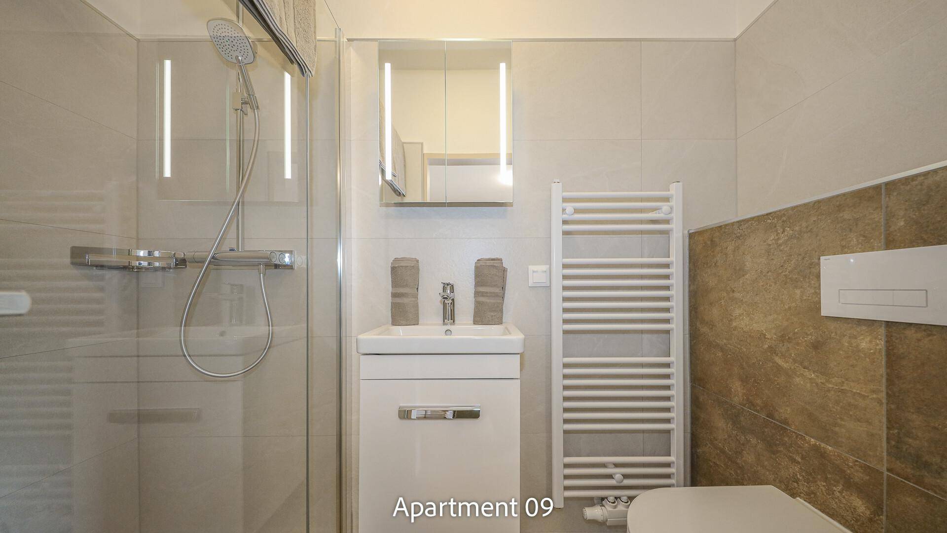 Modernes Badezimmer von Apartment 09 mit hellen Fliesen, Waschtisch, WC und einer geräumigen Duschkabine.