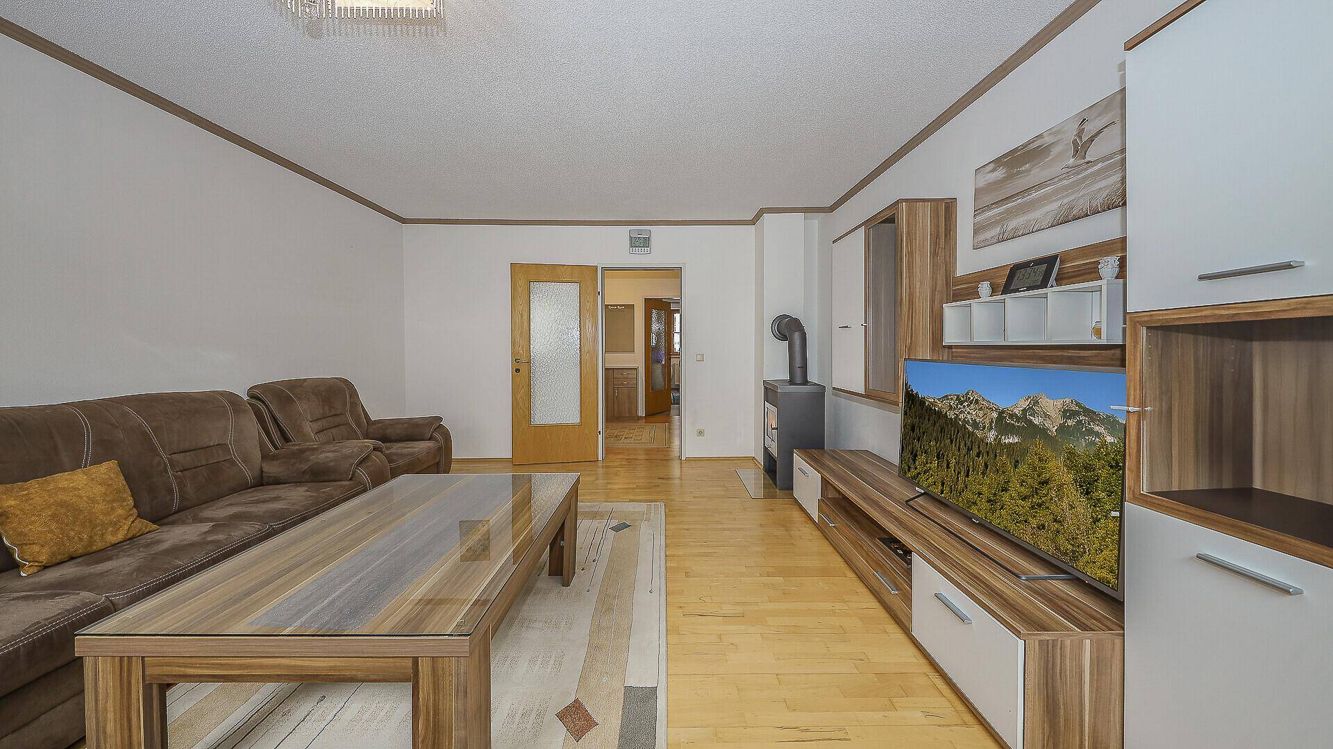 Helles Wohnzimmer mit Kaminofen, Sofa und Blick in den Flur.