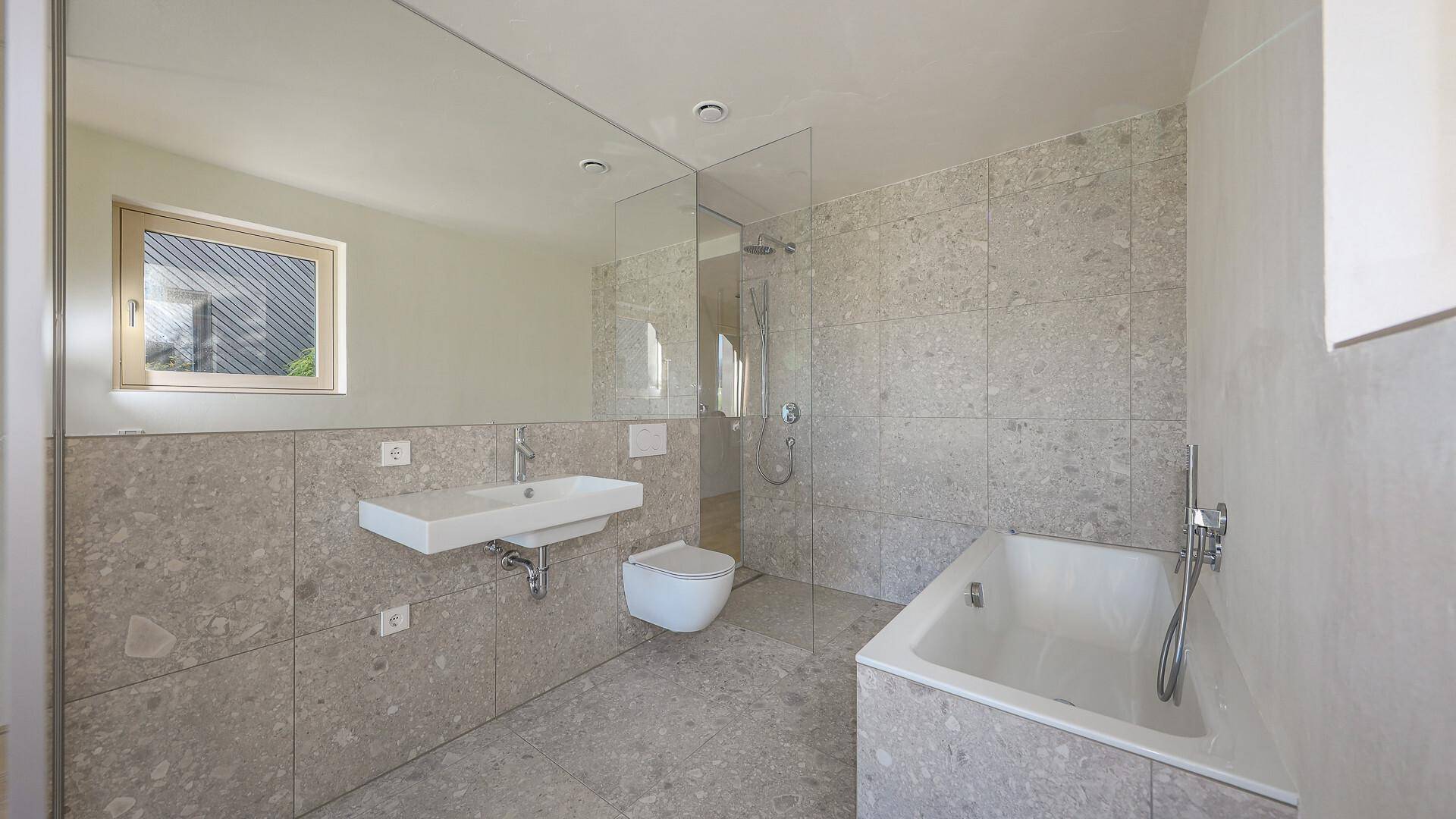 Modernes Badezimmer mit großformatigen Fliesen, Badewanne, Dusche und Fenster.