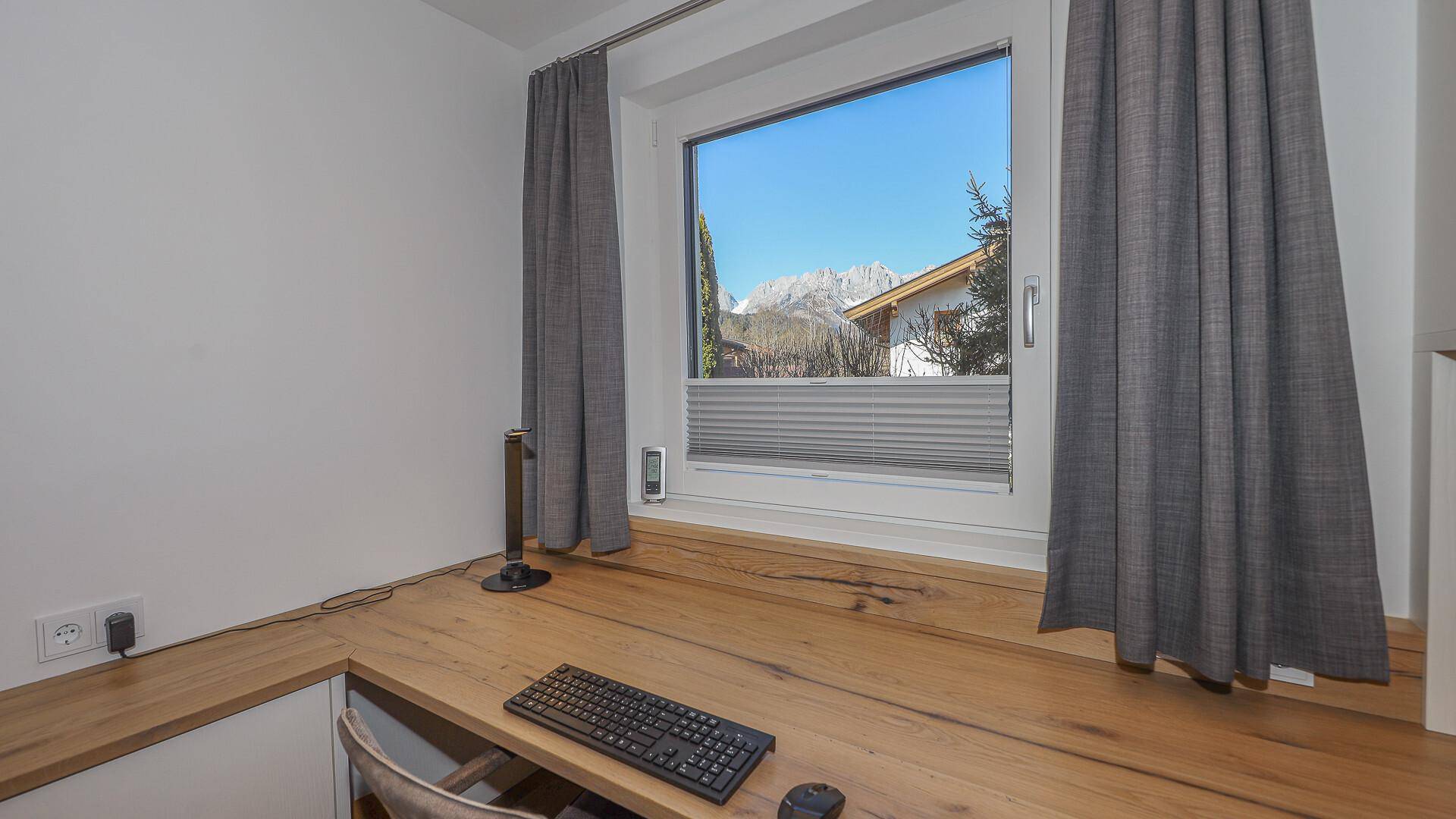 Arbeitsplatz mit Holzschreibtisch und Bergblick durch das große Fenster.