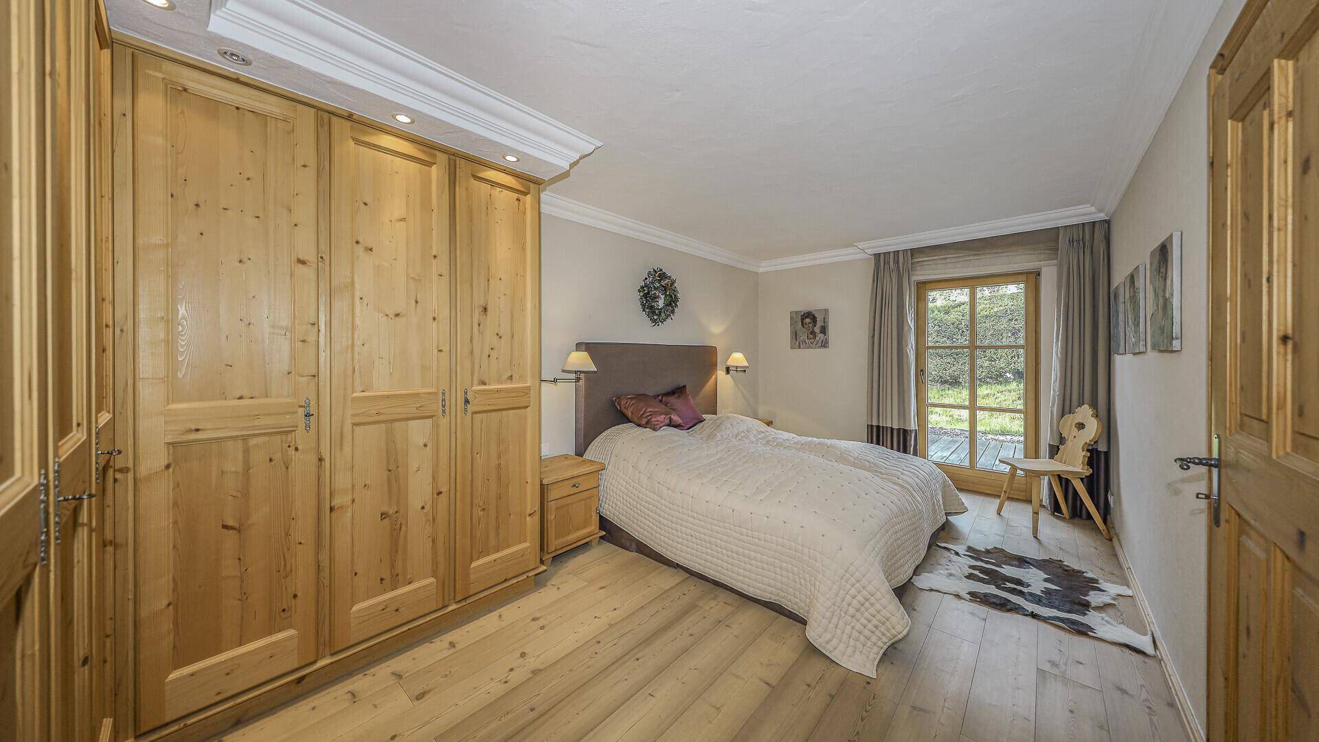 Helles Schlafzimmer mit Holzboden, Einbauschränken und Zugang zum Außenbereich.