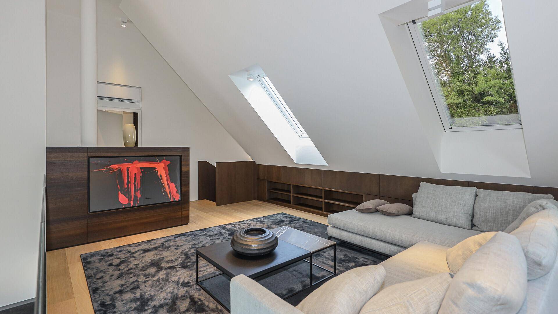 Geräumiges Wohnzimmer im Dachgeschoss mit modernen Möbeln, Dachfenstern und Holzboden.