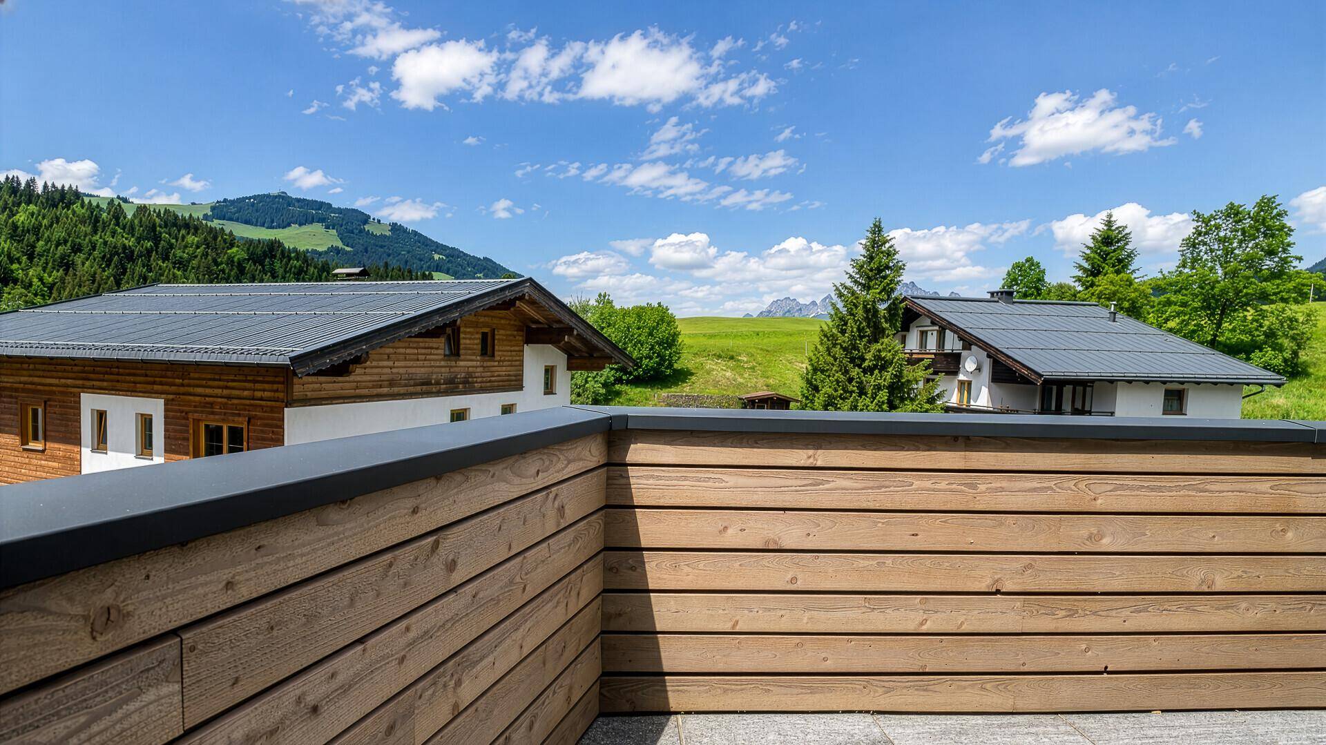 Weitläufiger Ausblick von der Terrasse auf grüne Hügel und die majestätische Berglandschaft.