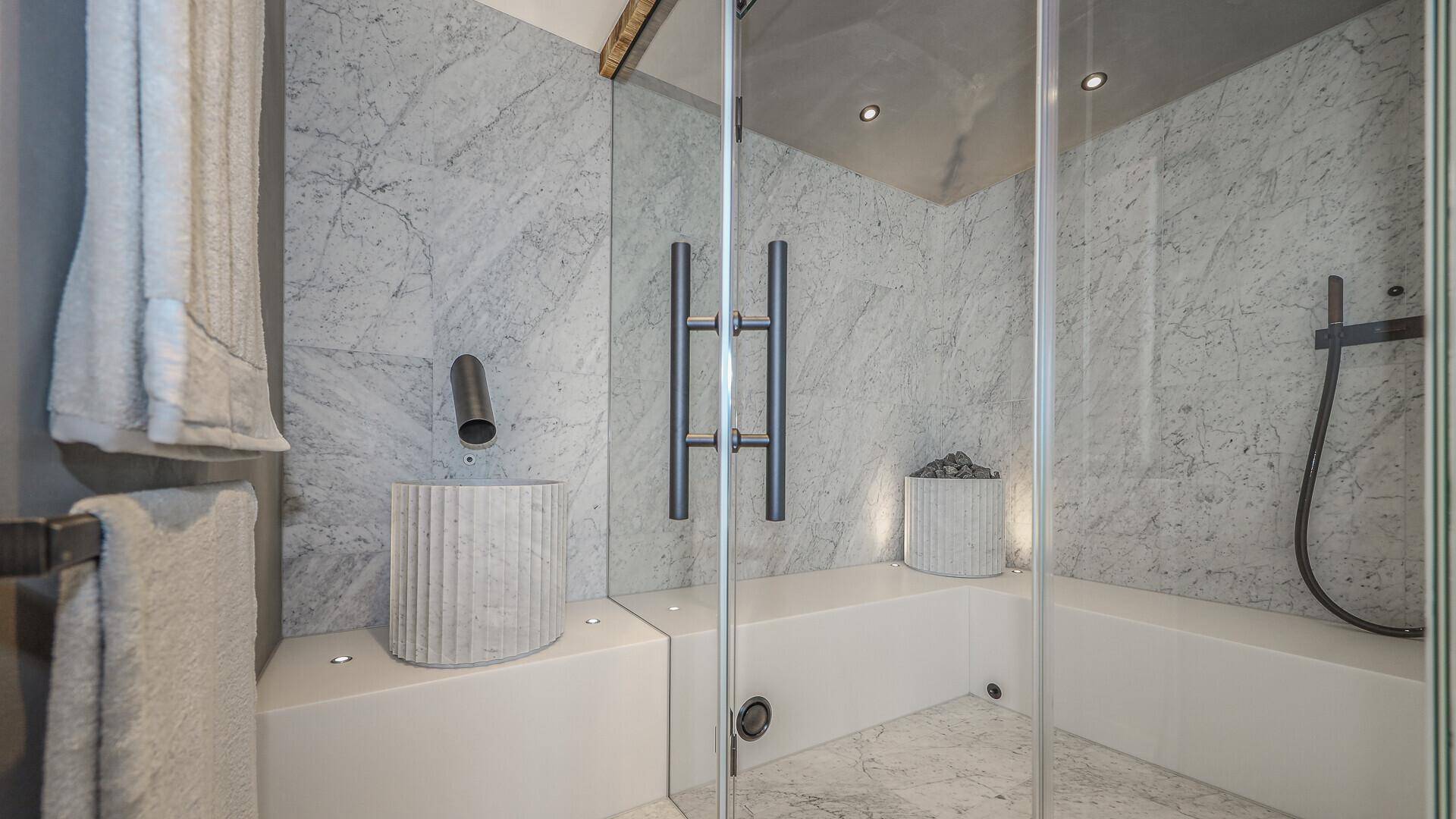 Moderne Dusche im Wellnessbereich mit Marmorwänden und stilvollem Design.