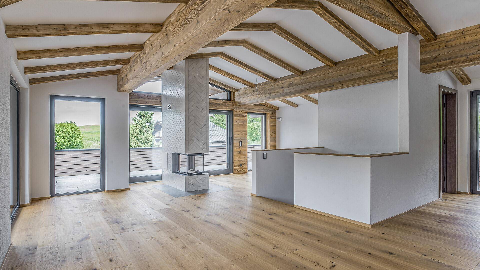 Geräumiges Wohnzimmer mit Holzbalkendecke, modernem Kamin und großen Fenstern mit Bergblick.