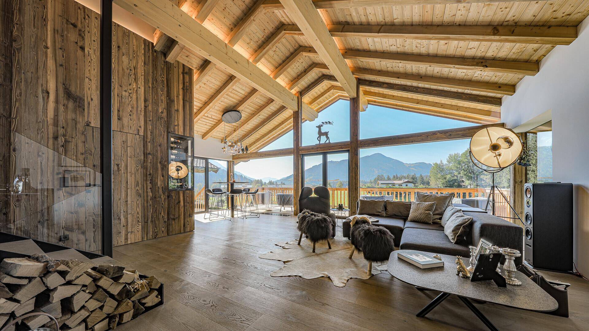 Gemütliches Wohnzimmer im alpinen Stil mit Holzbalkendecke, Kamin und Panoramablick auf die Berge.