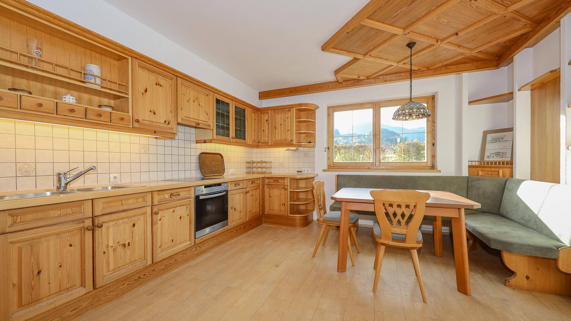 Traditionelle Holzküche mit Essecke, Fliesenrückwand und Blick auf die umliegende Landschaft.