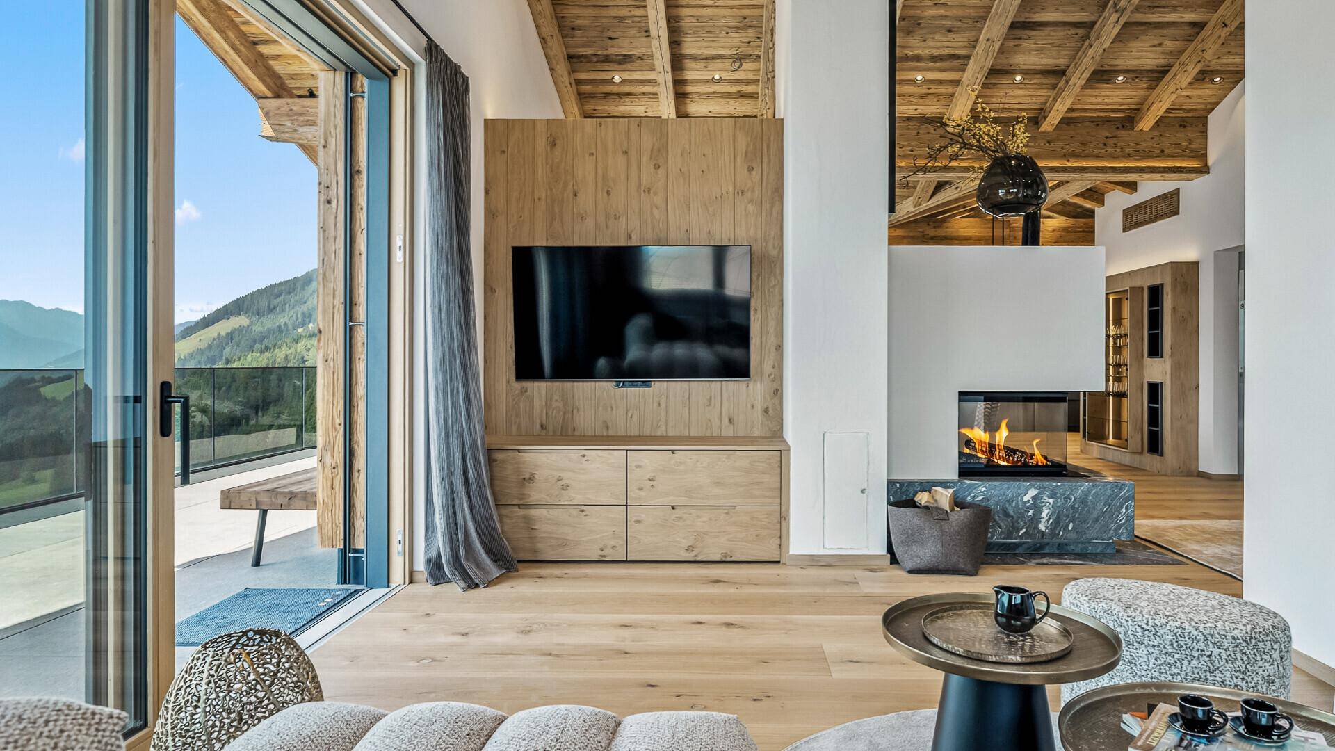 Moderner Wohnbereich mit Holzwand, integriertem Fernseher und Kamin, offen zum Essbereich.