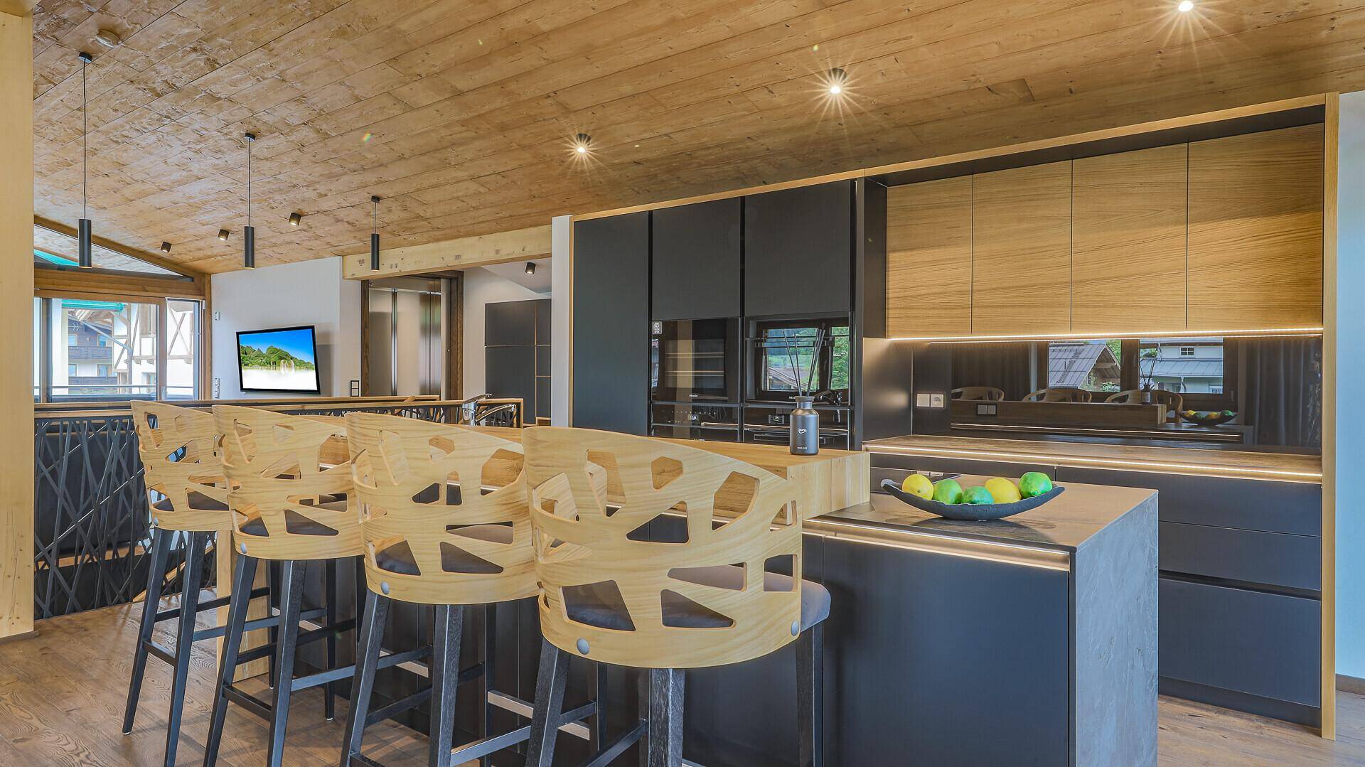 Moderne Küche mit dunklen Schränken, Holzdetails und einer Kücheninsel mit Barhockern.