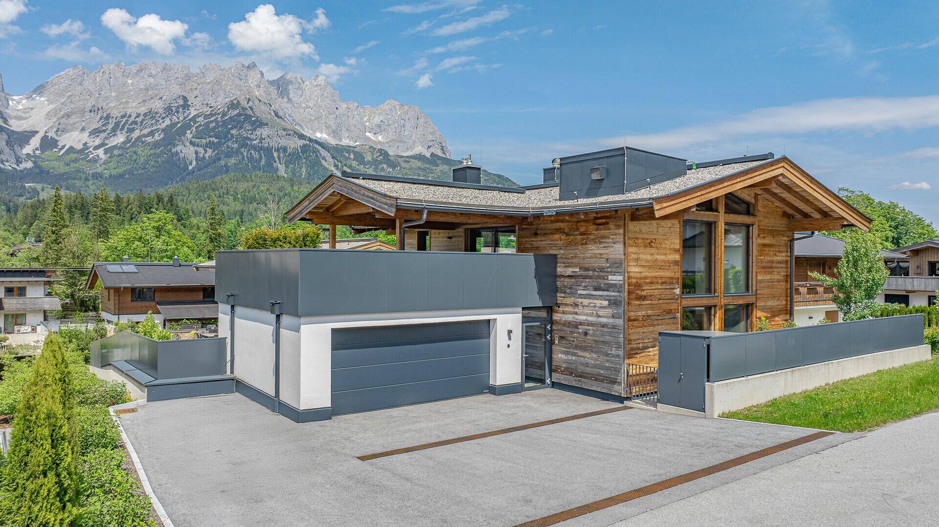 Elegantes Chalet mit Holzfassade, Doppelgarage und beeindruckendem Bergblick unter blauem Himmel.
