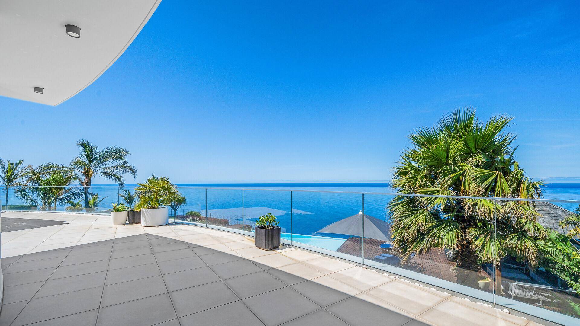 Große Sonnenterrasse mit Glasgeländer, weitem Meerblick und angrenzendem Poolbereich.