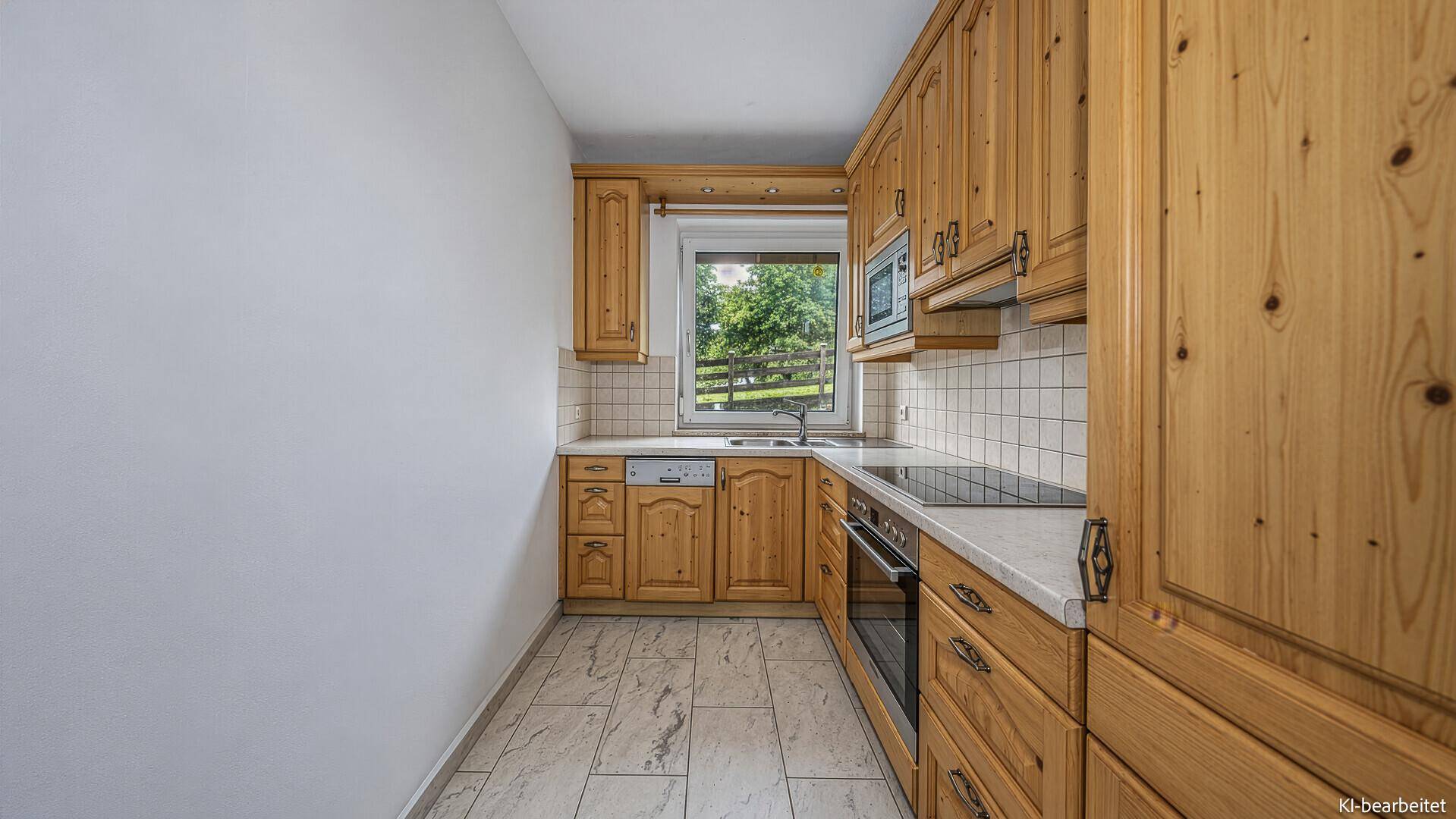 Traditionelle Küche mit Holzschränken, Fliesenboden und Blick ins Grüne durch das Fenster.
