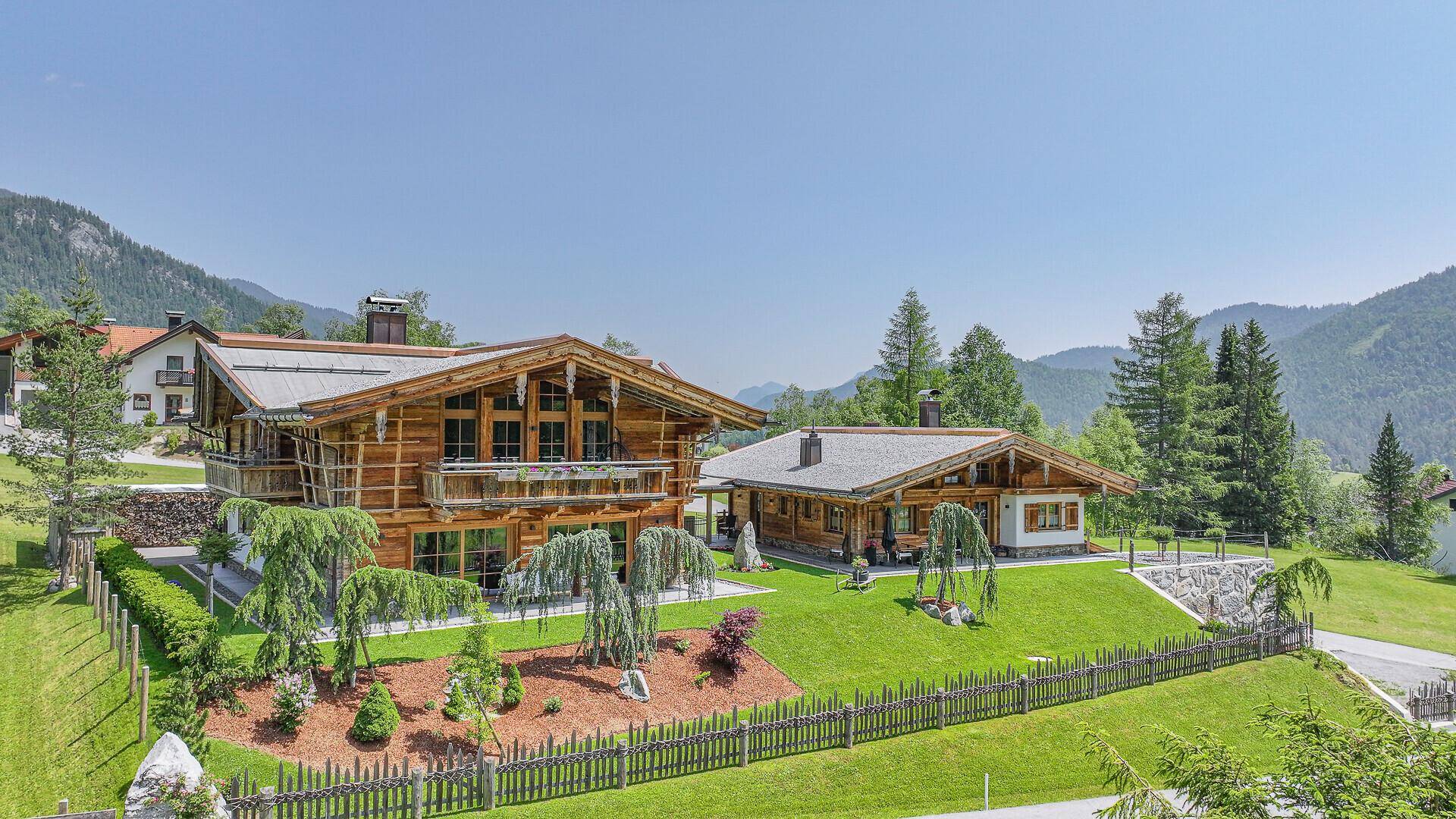 Zwei traditionelle Chalets mit Holzbalkonen und gepflegten Gärten in einer idyllischen Berglandschaft.