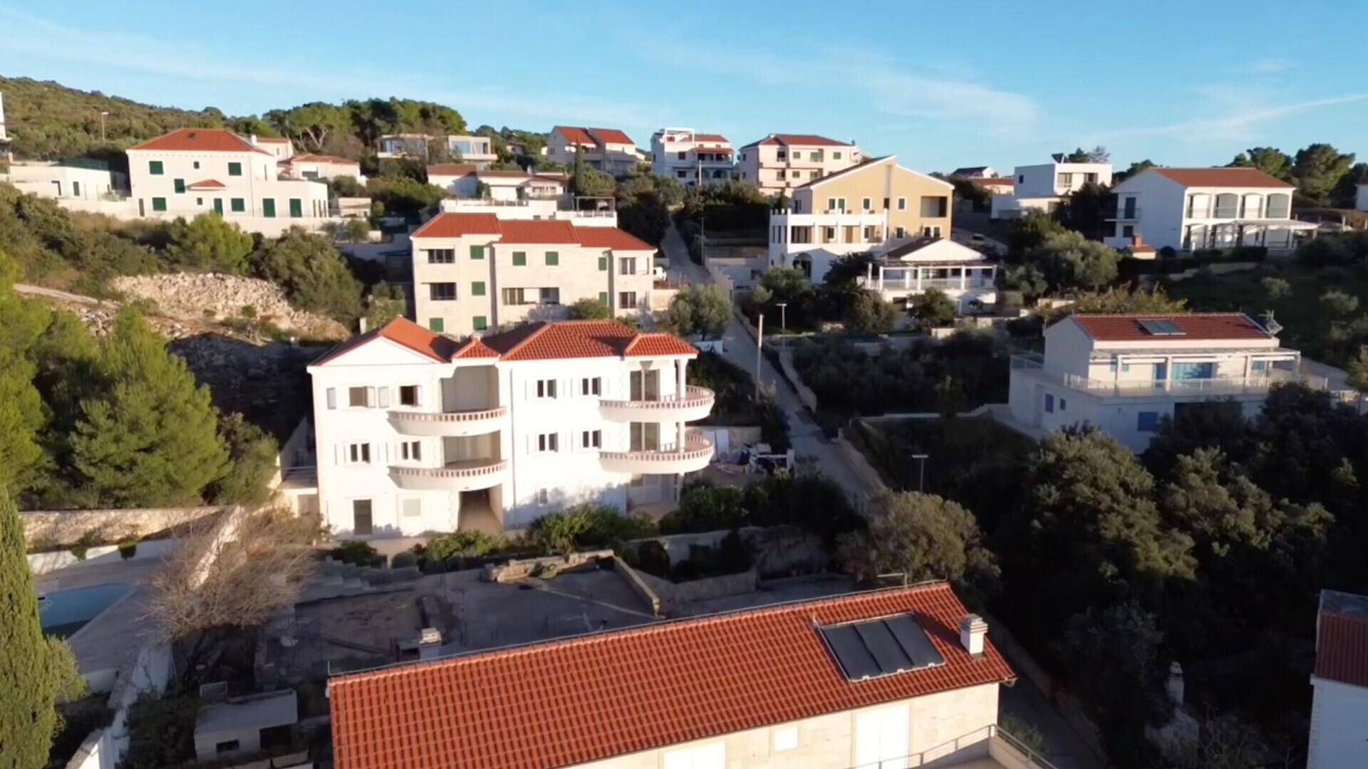Wohngebiet mit vielen Häusern und grünen Hügeln unter klarem Himmel, einige mit Solaranlagen.