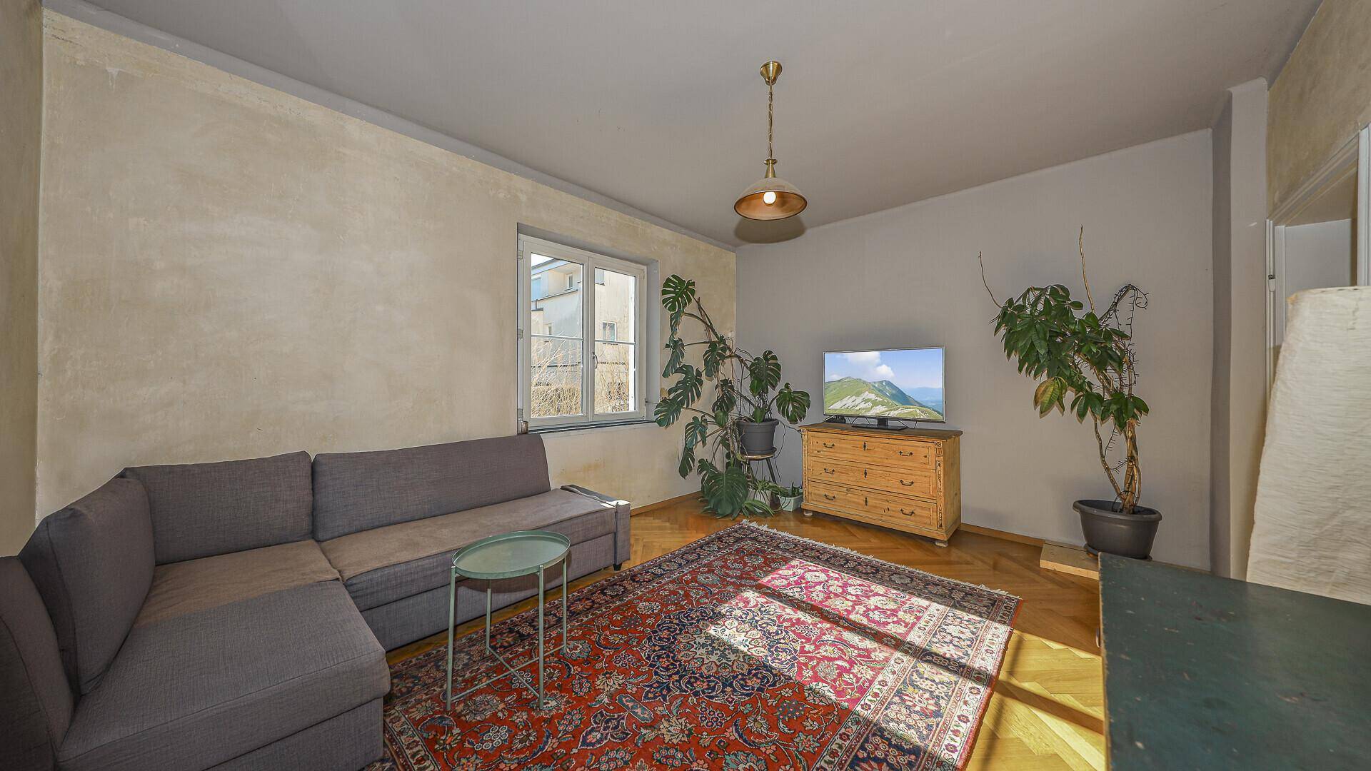 Gemütliches Wohnzimmer mit Ecksofa, Holzboden und Blick ins Grüne.